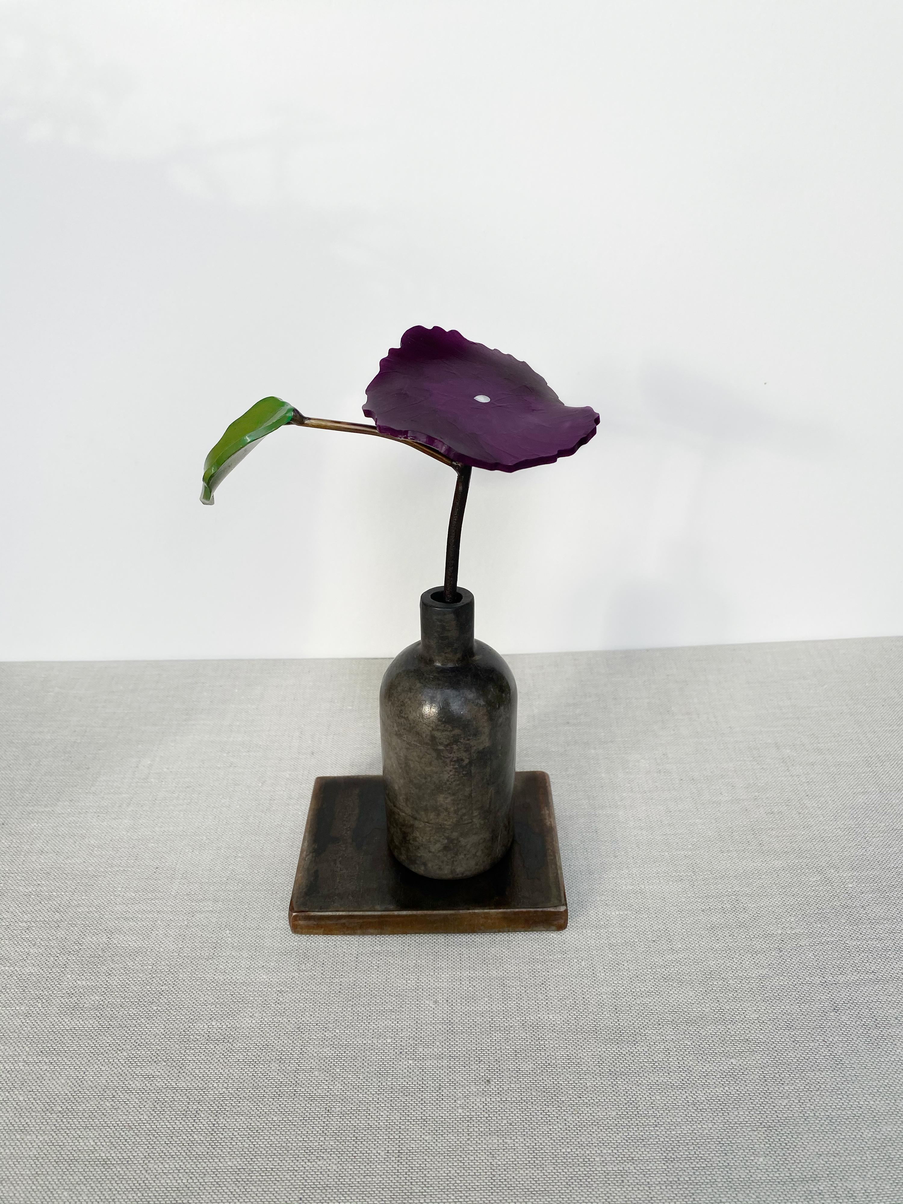 'Morning Glory' by David Kimball Anderson, 2020. Bronze, steel, and paint, 8 x 4 x 3 in. This sculpture features a round vase cast in bronze and finished in varying patinas of light and dark gray. The flower is in a bright color of purple and one