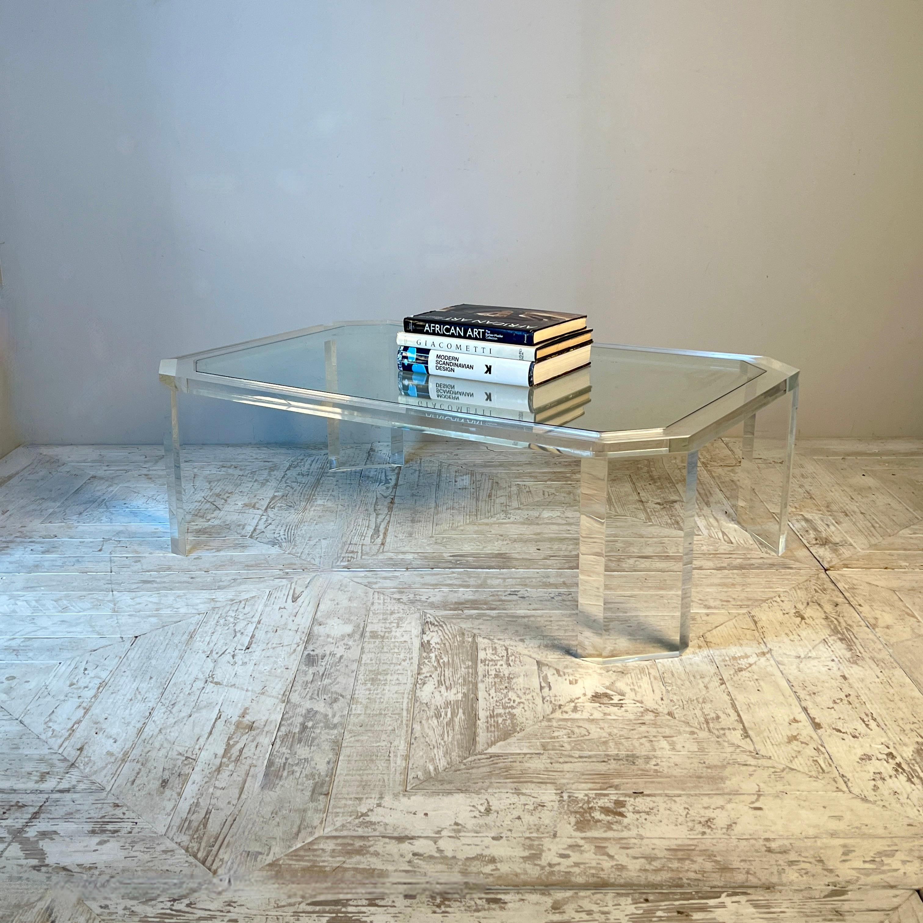 A sleek and stylish 1970s David Lange Lucite coffee table featuring a rectangular design with canted corners and an inset glass top. Supported by angled Lucite legs that mirror the table’s shape, this timeless piece adds functionality while allowing