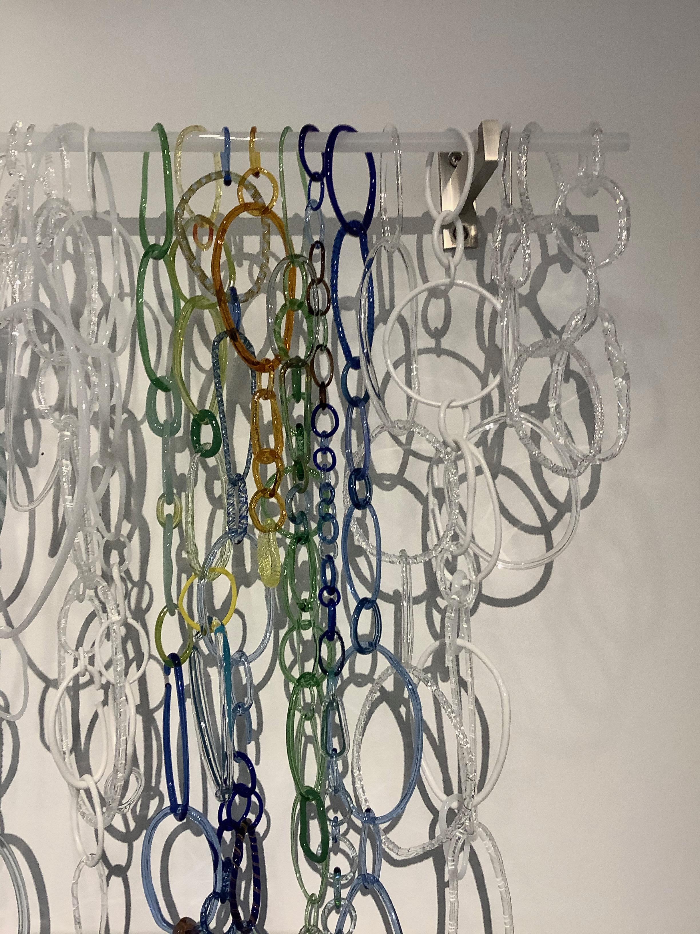 This hanging sculpture by David Licata is composed of free-form circular and oval loops of torch-worked borosilicate glass in white, clear, green, cobalt, golden orange, yellow and golden pink. The loops, in varying sizes and textures, cascade