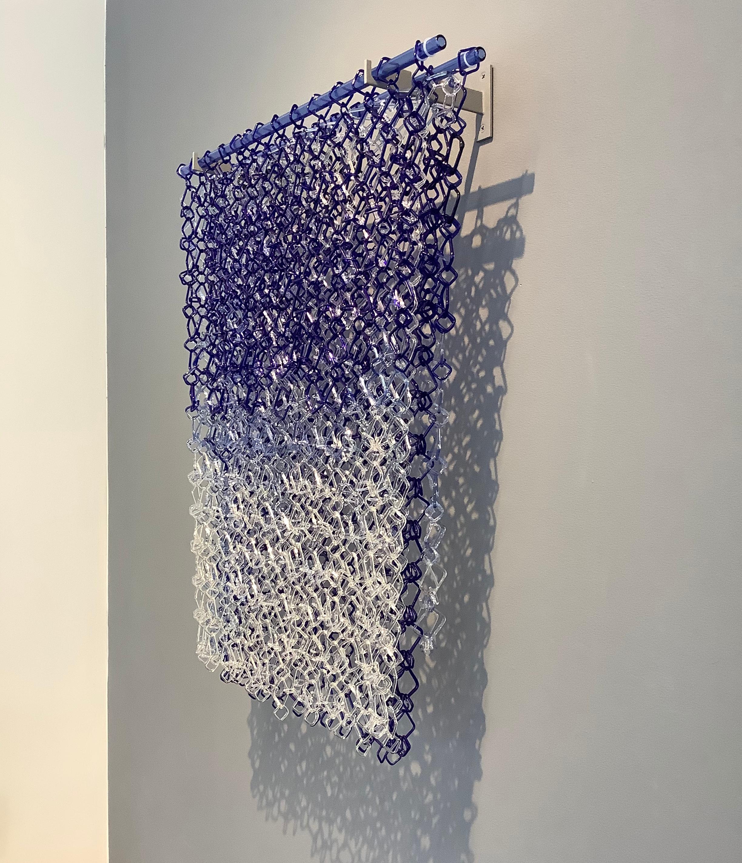 This hanging sculpture by David Licata is composed of square links of torch-worked borosilicate glass in shades of blue from dark cobalt at the top, pale translucent violet in the middle and clear links at the bottom.  The square links are joined