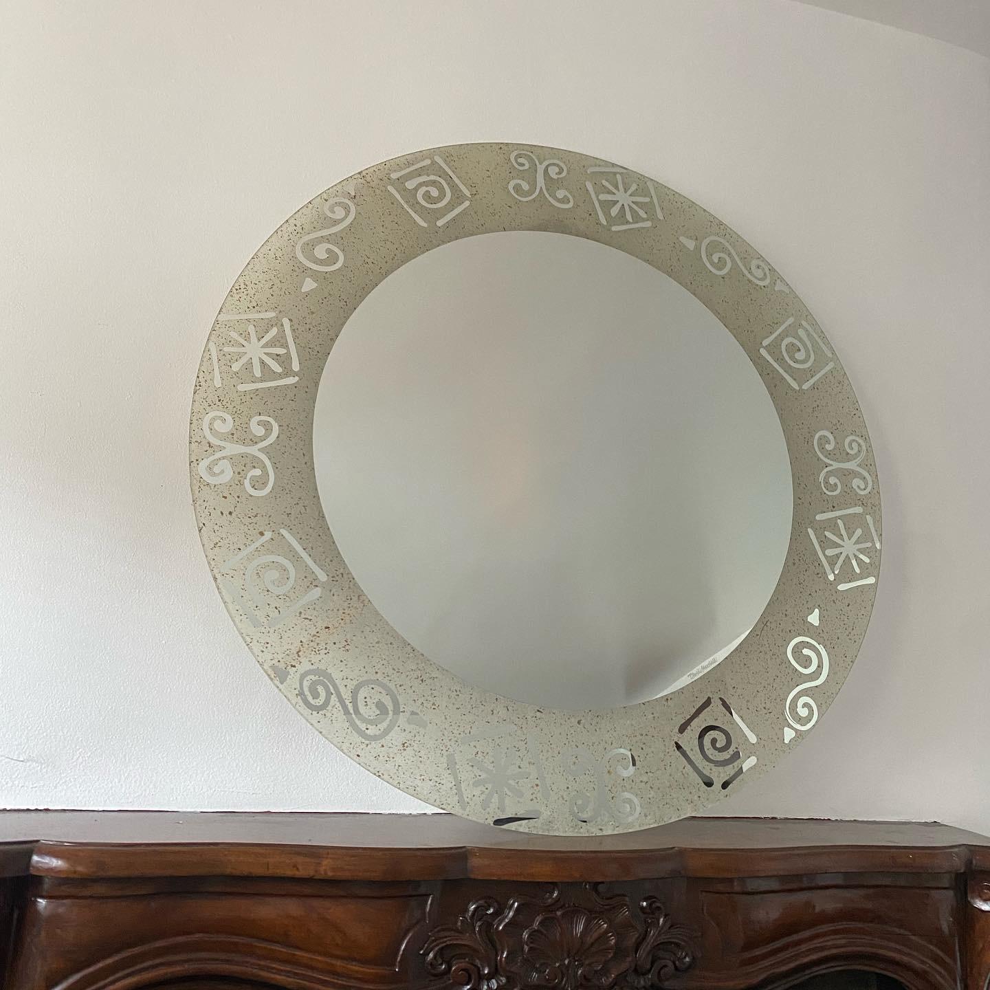 David Marshall signed large round mirror is a striking piece of art that will elevate any space in which it is displayed. The center mirror is framed by abstract symbols around perimeter with spotted gilt and copper leaf flecks, truly unique piece