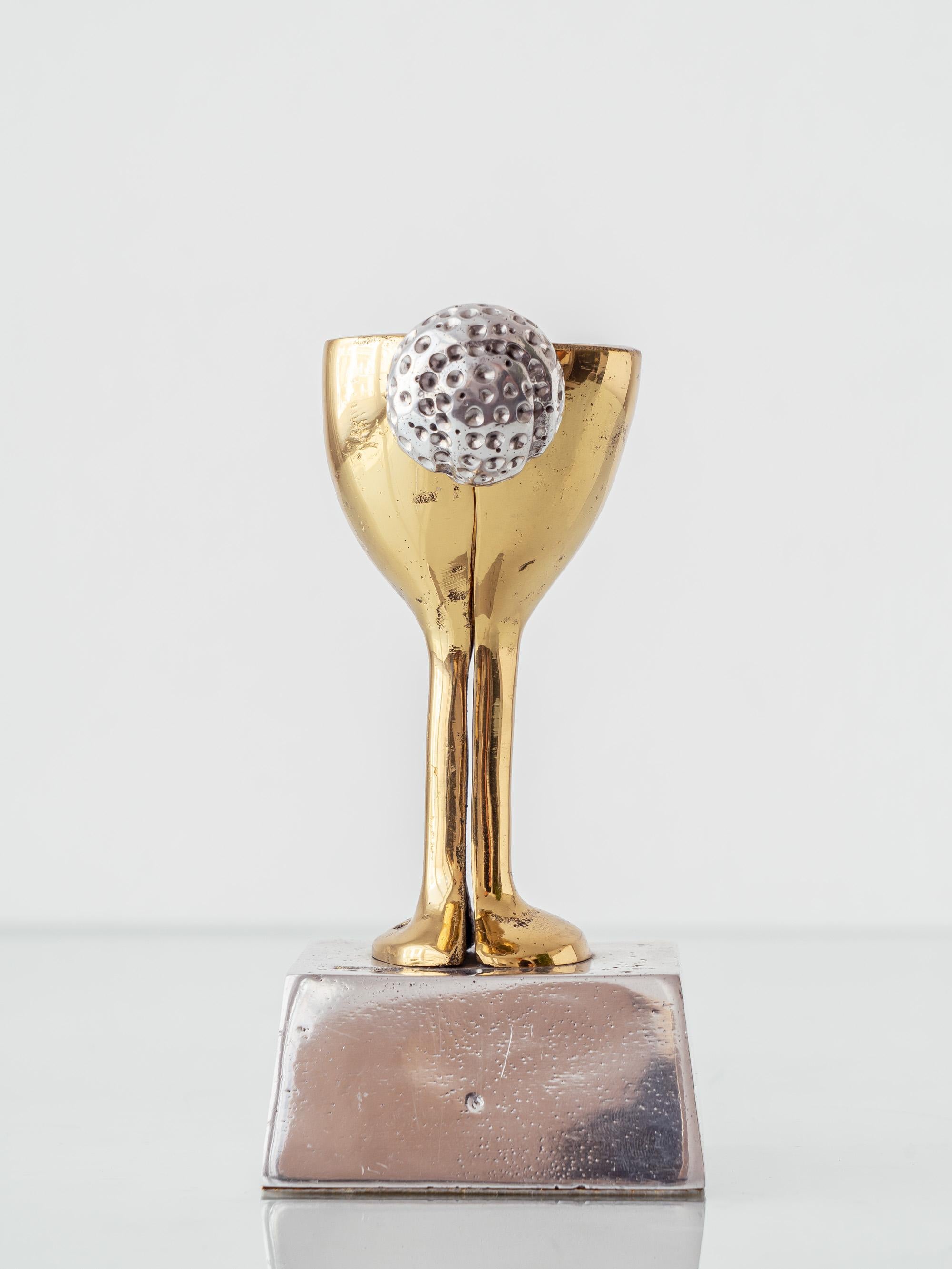 Golf trophy sculpture by David Marshall, in cast brass and aluminum, expressed in his unmistakable Brutalist vocabulary. The goblet-form cup (gold-toned brass) features a split rim and an applied, silver-toned dimpled golf ball; it rises from a