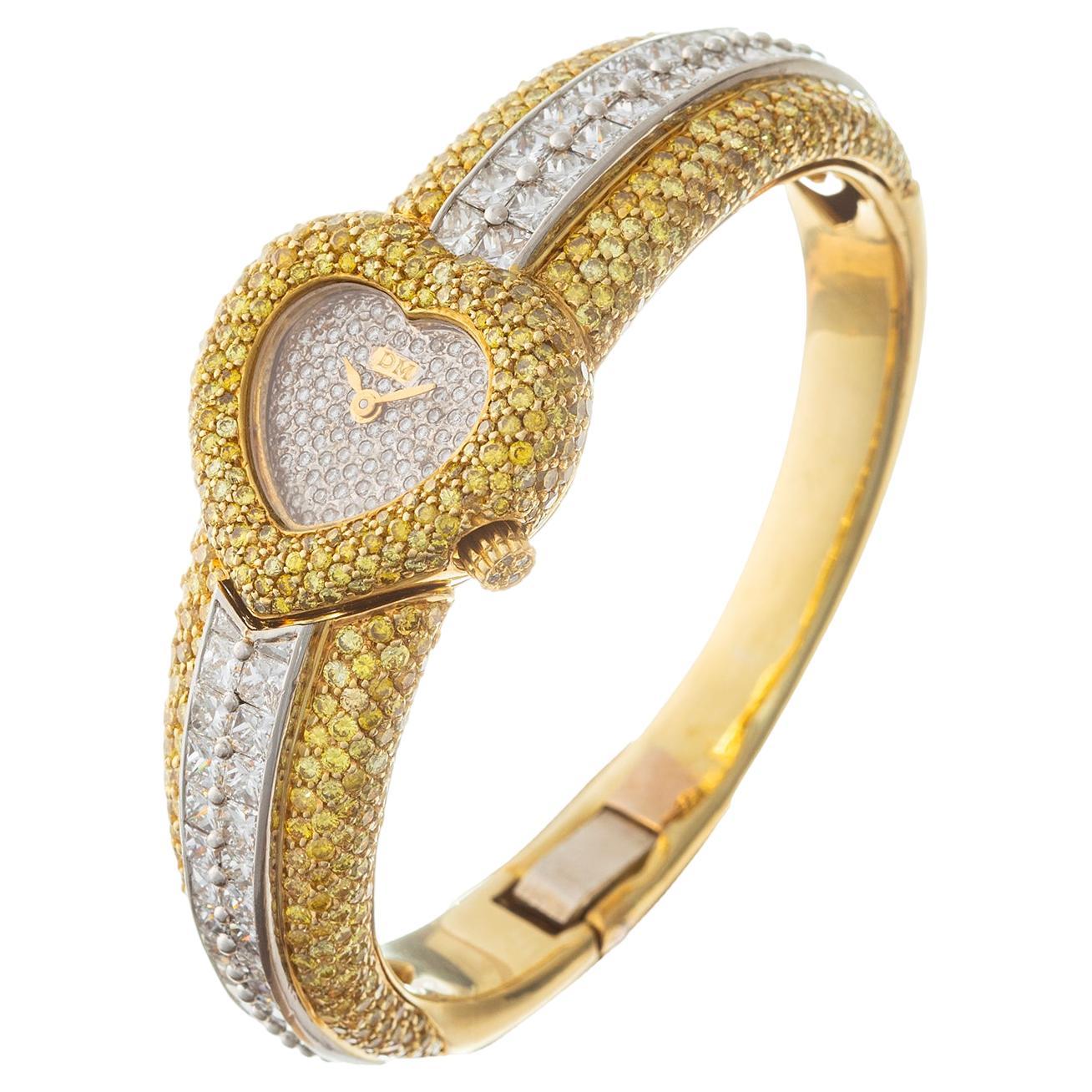 Ladies' fancy intense yellow diamond and white diamond bracelet watch in 18k yellow gold, featuring a quartz movement by Piaget; pavé-set white diamond dial; pavé-set round-cut natural fancy intense yellow diamond heart-shaped case. Bangle-style