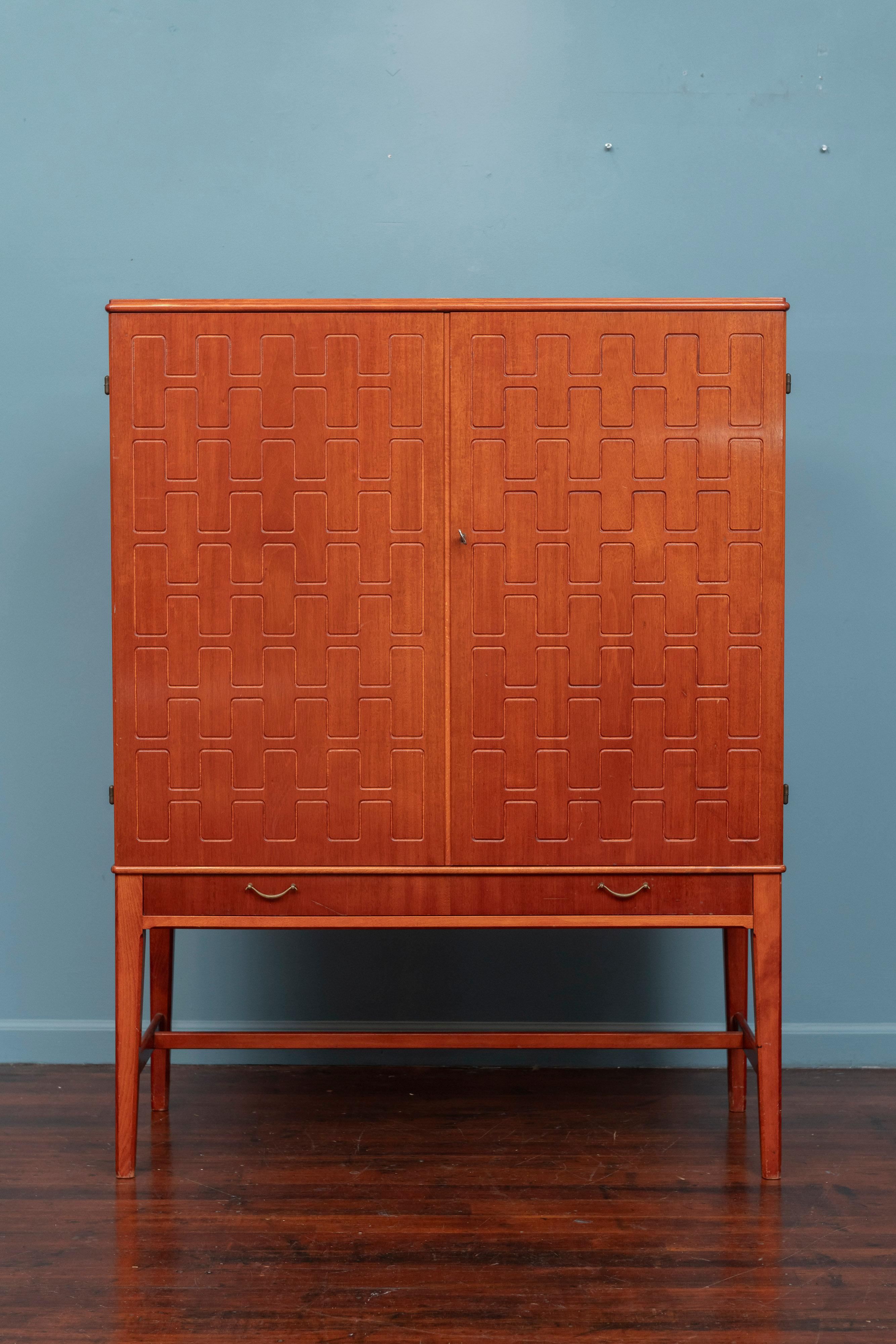 Armario sueco de teca y caoba, circa años 50. Diseñado por David Rosén y fabricado por Svensk Möbelindustri. La parte superior rectangular sobre dos puertas de armario con un diseño clásico tallado en relieve en las puertas, encima de un cajón largo