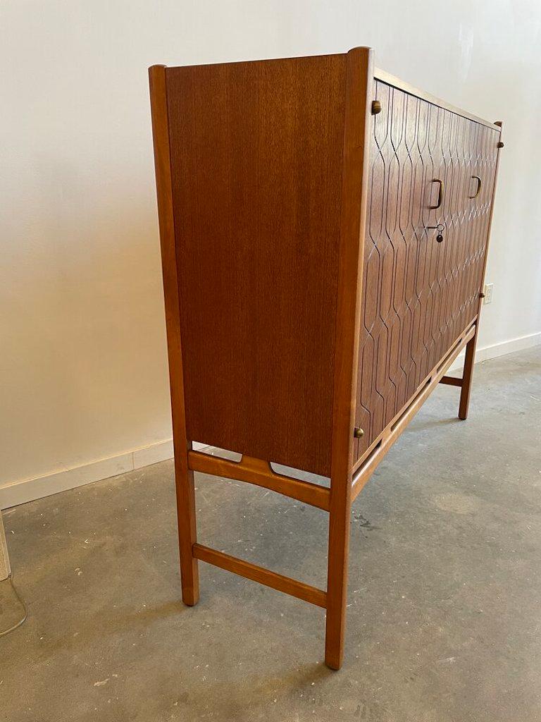 David Rosen sideboard for Nordiska Kompaniet with four felted drawers and two storage cabinets with brass detailing and working lock and key. This hand etched sideboard is made from solid teak wood.

 