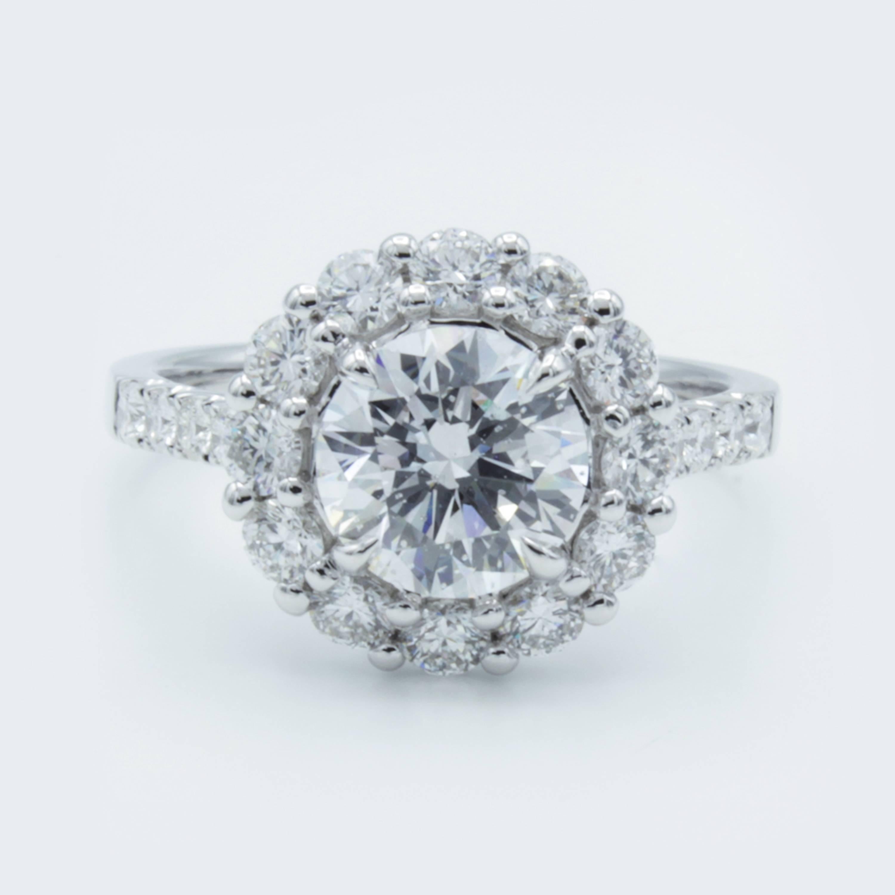 A beautiful flower blossoms in this Rosenberg Diamonds & Co. engagement ring. A GIA certified 1.54 carat round brilliant cut diamond rests surrounded by glittering white pave set diamond accents within a band of 18Kt white gold. Designed by David