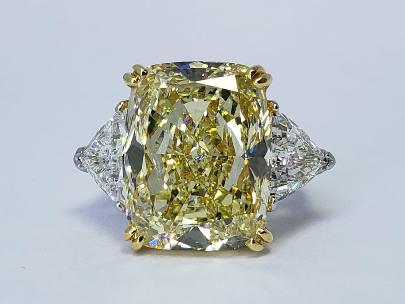 An exceptional Rosenberg Diamonds & Co. ring presenting an incredible GIA certified 16.48 carat fancy yellow cushion cut diamond upon a band of bright platinum and 18Kt yellow gold. The center stone is flanked by trillion side stones with a total