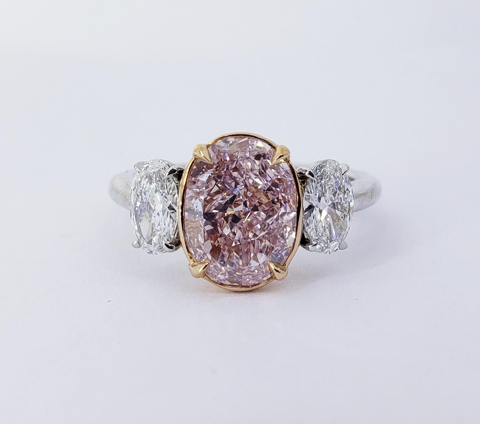 Rosenberg Diamonds & Co. 2.67 carat Oval cut Fancy Pink Purple VVS1 clarity is accompanied by a GIA certificate. This spectacular three stone rare pink diamond is set in a handmade platinum and 18k yellow gold setting with perfectly matched pair of