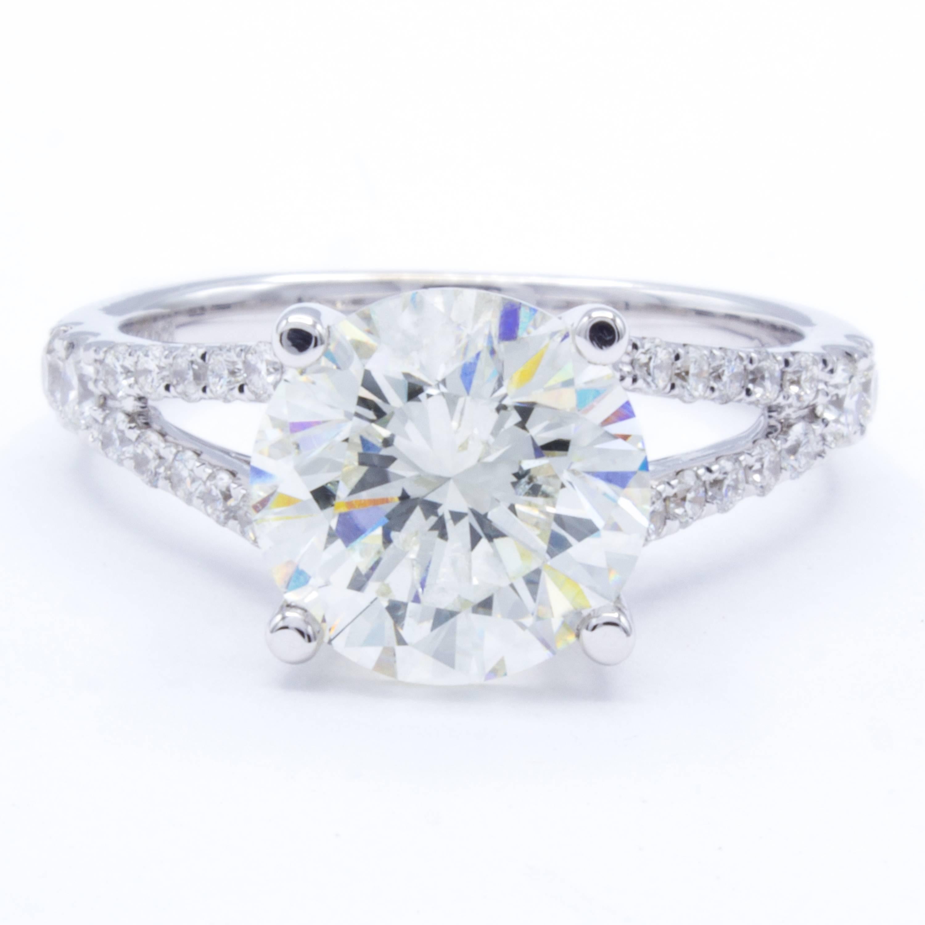 An exceptional diamond engagement ring shows a split shank band of 18kt white gold. All across the band shine round brilliant pave set diamond accents. At the center, a scintillating 2.87 carat round brilliant diamond sends fiery motes in every