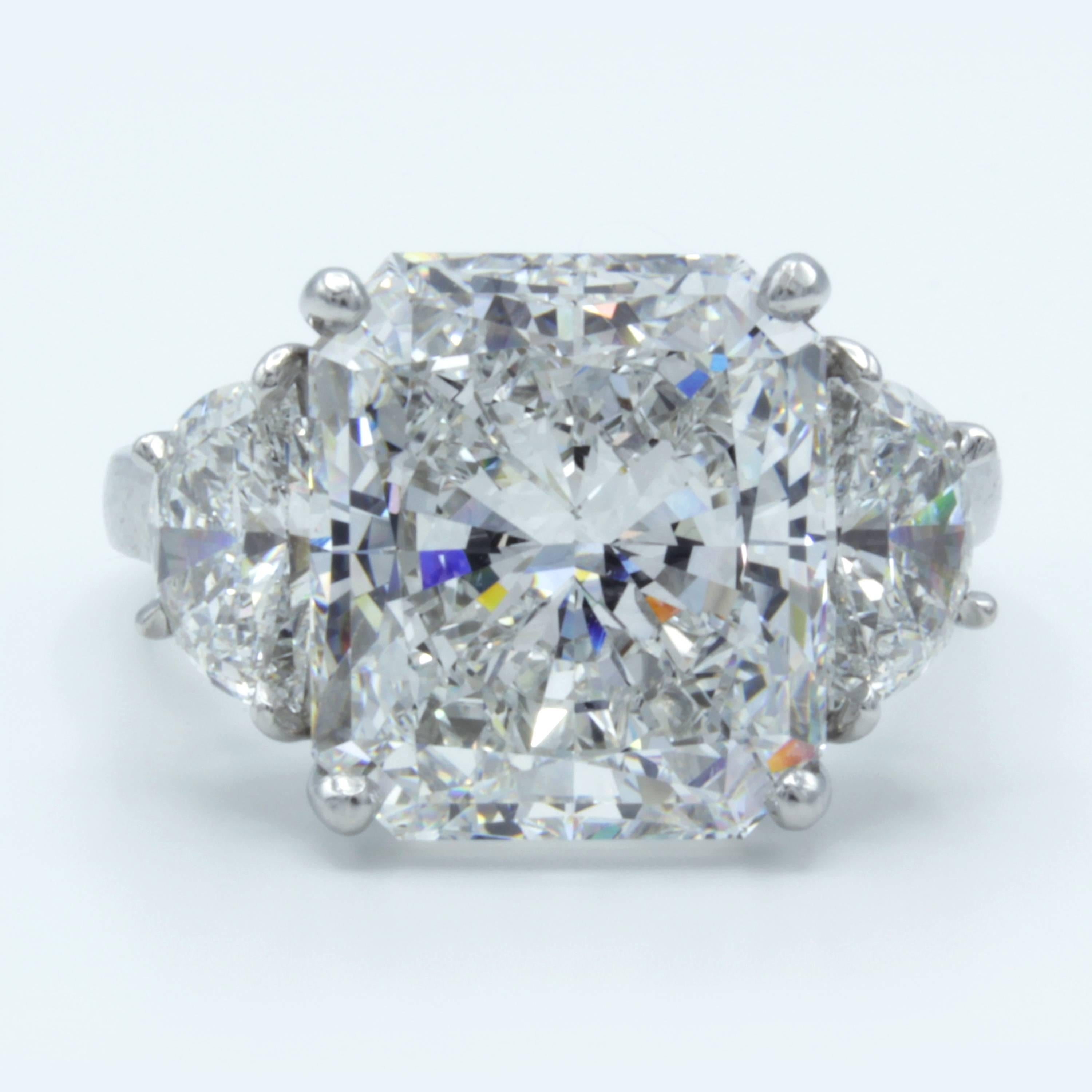 A Rosenberg Diamonds & Co. GIA certified 7.11 carat radiant cut diamond reveals swathes of prismatic color in a range of fiery flashes from within a setting of bright platinum. At both sides rest gleaming half-moon side stones of otherworldly