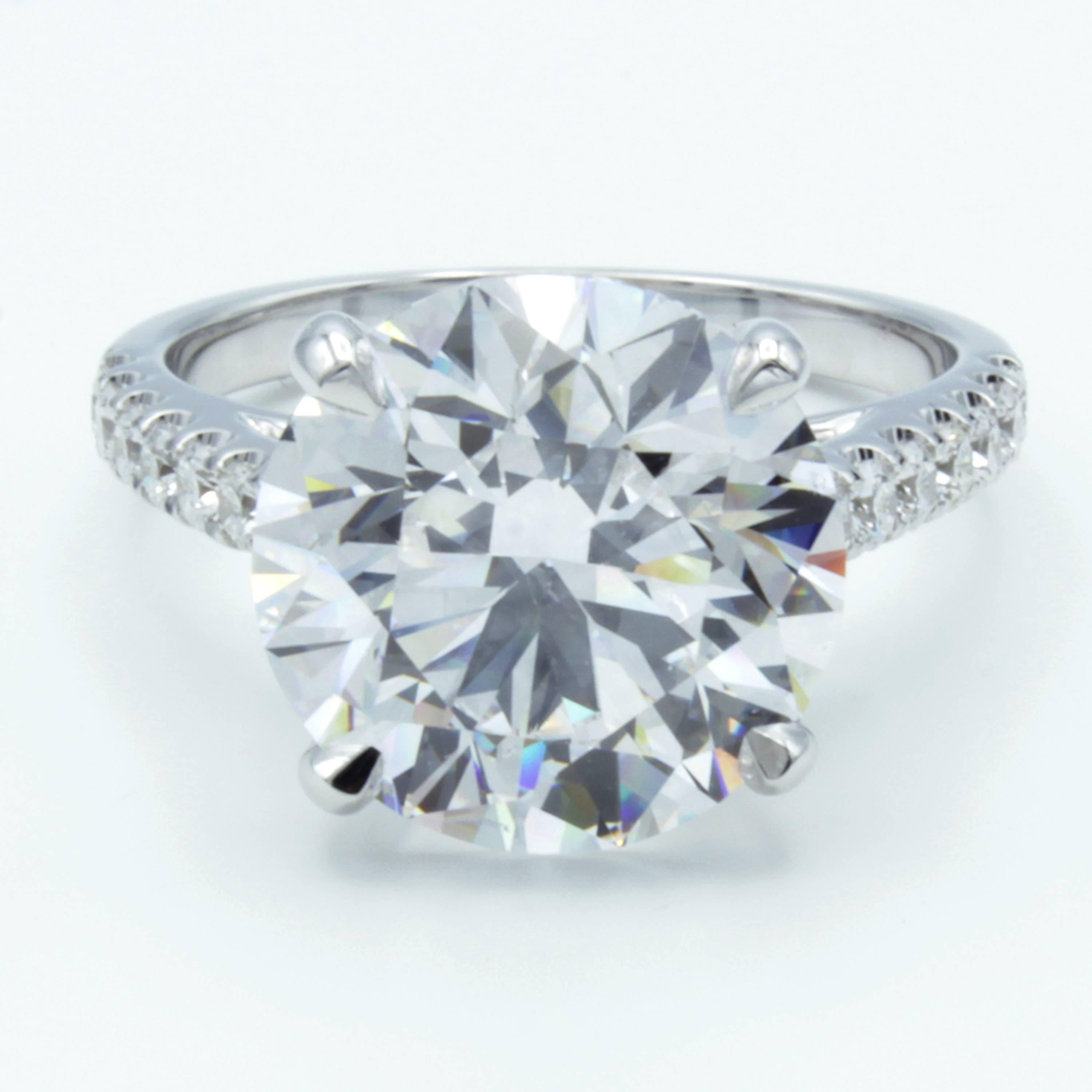 A classic Rosenberg Diamonds & Co. engagement ring shows a traditional design featuring a GIA certified 6.00 carat round brilliant diamond upon a band of bright 18K white gold. An elegant setting carries pave set diamond accents halfway around the