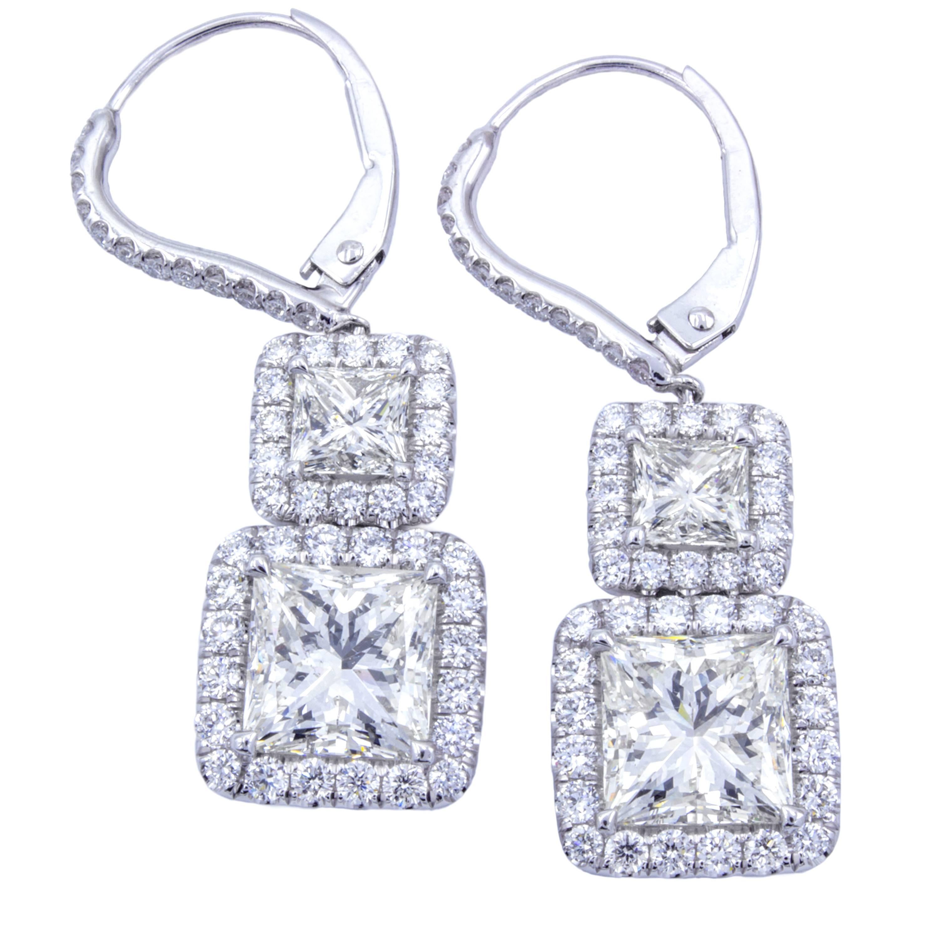 A pairing between incredibly fiery princess cut diamonds shows in a gorgeous pair of dangle drop earrings by Rosenberg Diamonds & Co. Platinum settings feature halo's of glittering round brilliant pave diamonds surrounding over 5 carats of princess