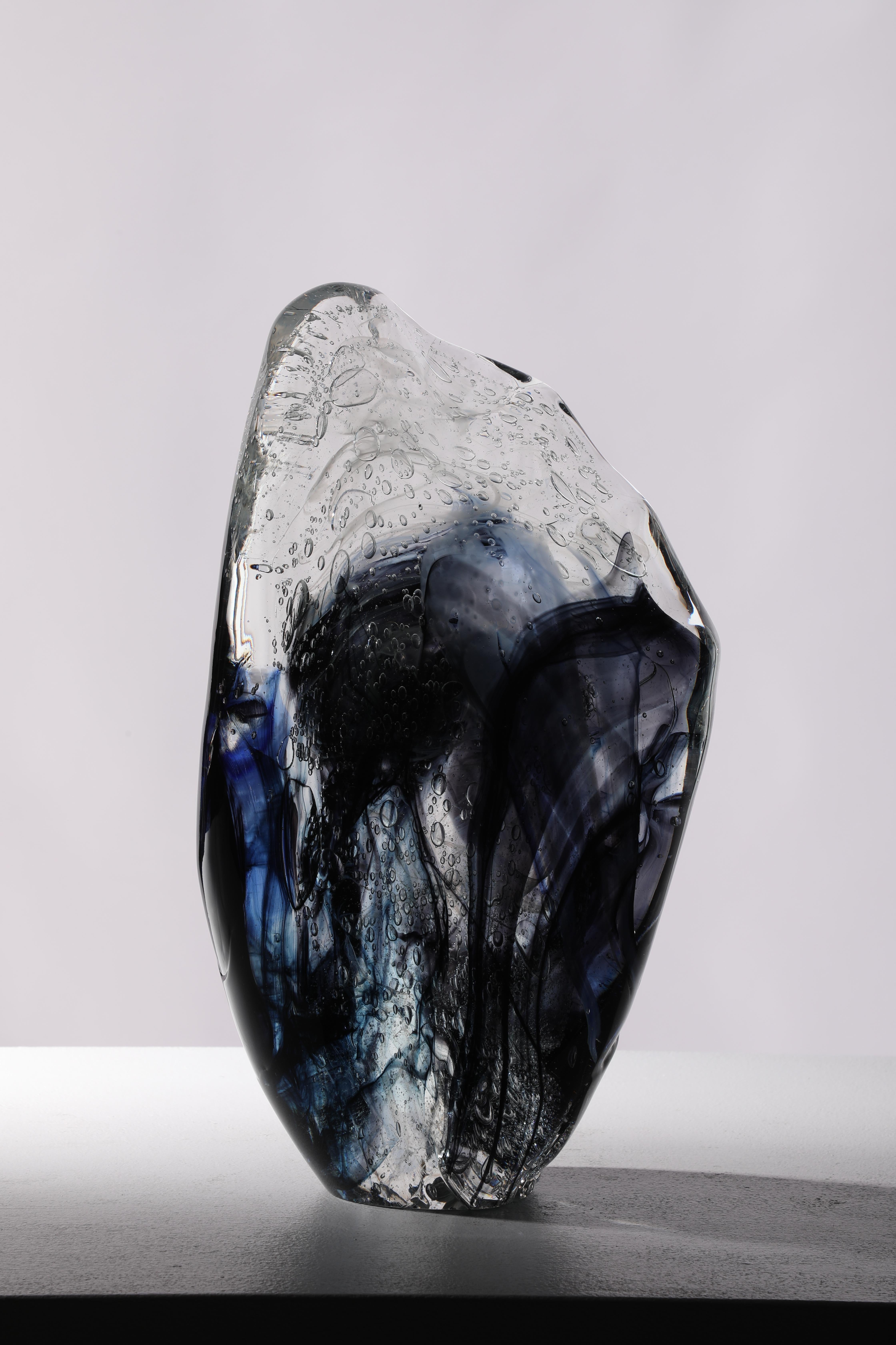'Alcaid' is a contemporary abstract cast glass sculpture by David Ruth from his Internal Space series. It is made by heating the glass and then hand working it into form. The main colors of black and dark blue contrasts the clear and white glass.