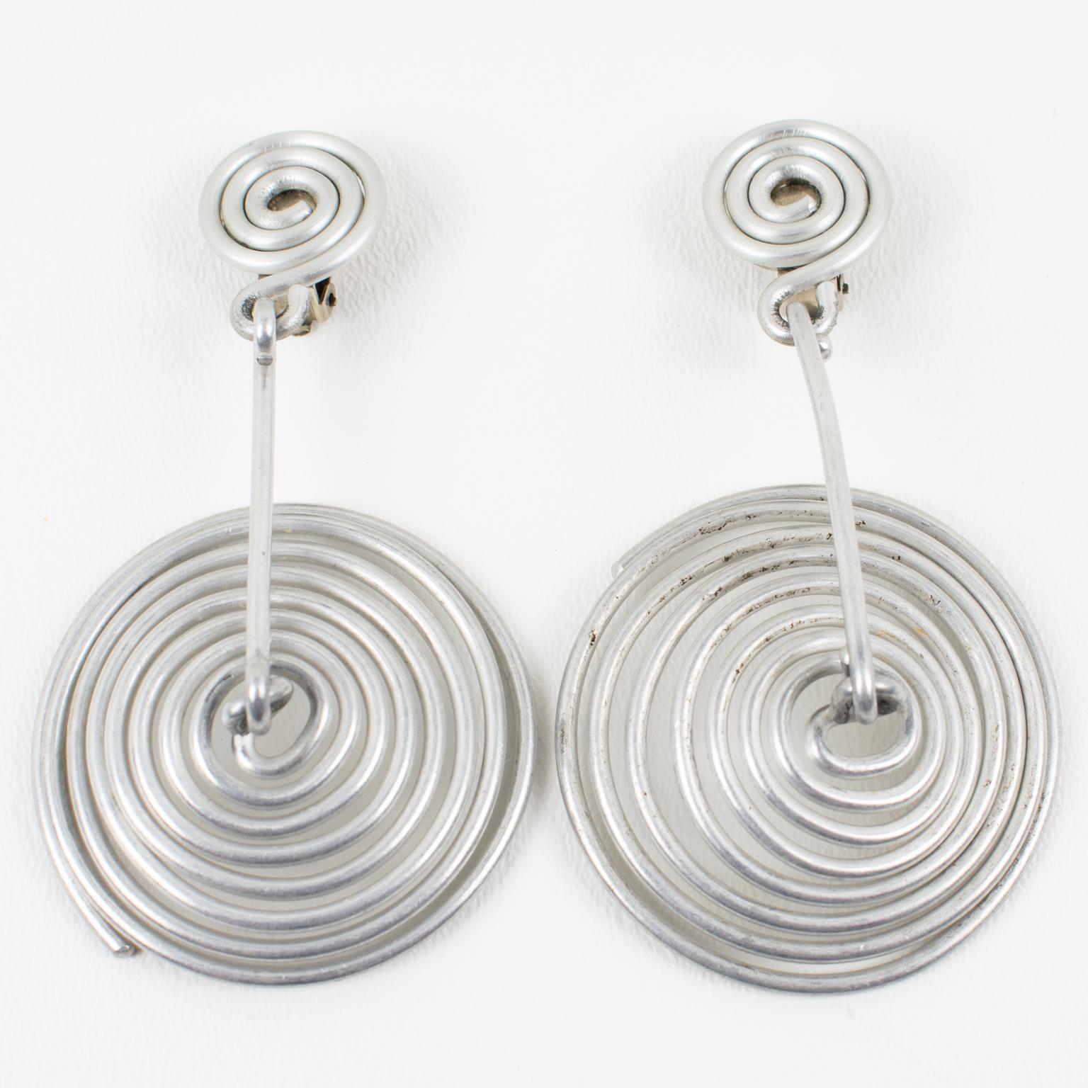 These rare modernist David Spada New York oversized clip-on earrings feature a striking Space Age 1980s design with a dangling articulated flat umbrella spiral coiled shape. They are made of anodized aluminum metal in silver color. Each earring is