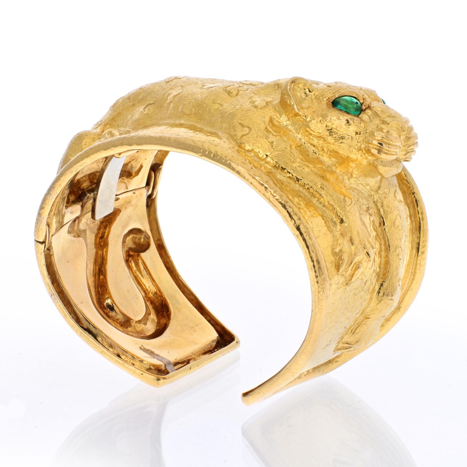 David Webb 'Repoussé Leopard' cuff bangle crafted in 18 karat yellow gold with enchanting emerald eyes. . Repoussé leopard cuff bracelet set with two pear-shaped emerald eyes, the emeralds weighing 0.7 total carats, in textured 18k yellow gold.