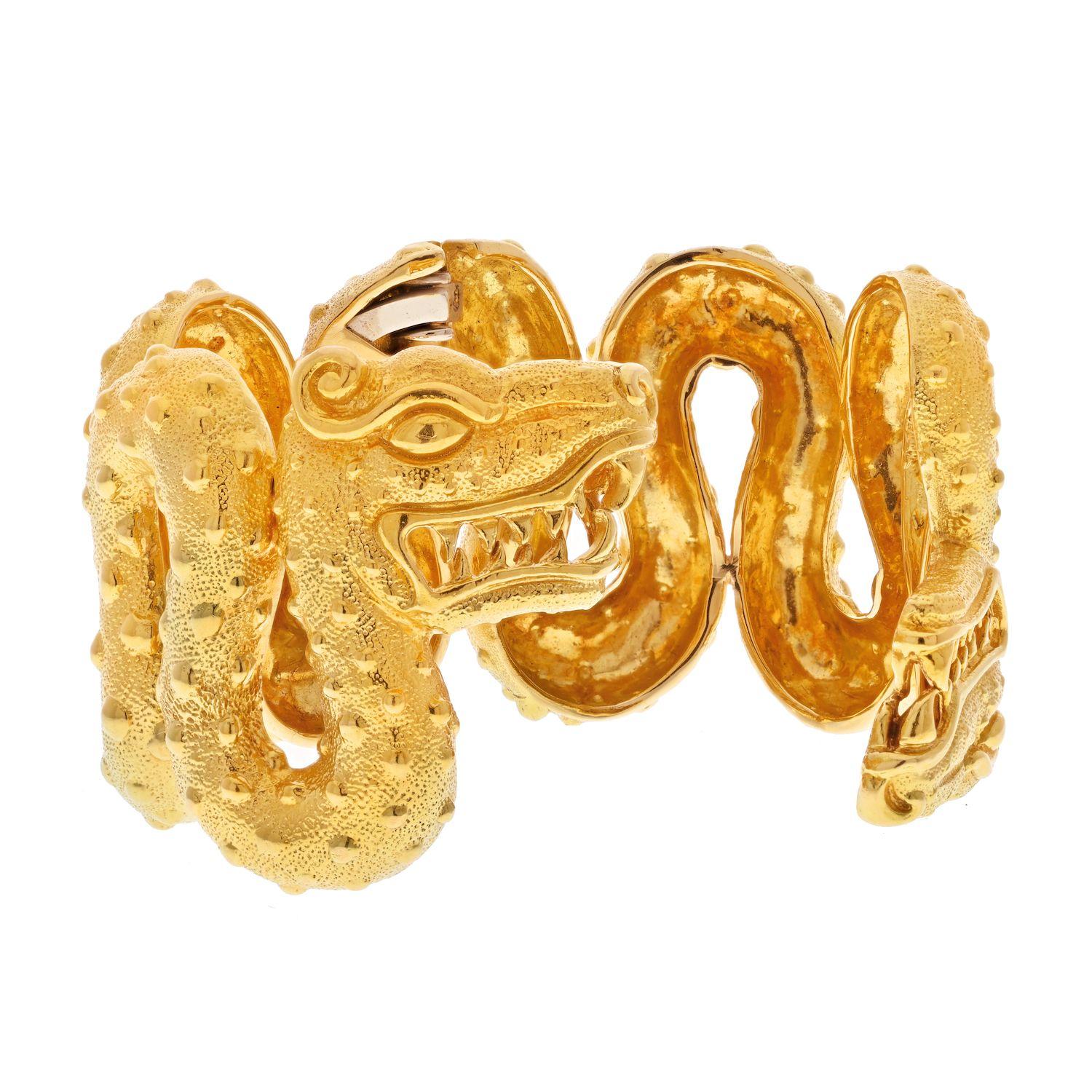 David Webb 18K Yellow Gold Aztec Cuff Double Dragon Head Bracelet.
Bracelet is designed with dragon head terminals and curvilinear texturous swirling body. With deeply grooved expressive facial features and raised spots throughout. Opens on a hinge.