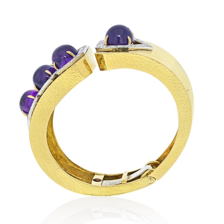 Designed as a wide textured yellow gold hinged cuff, set with four  oval cabochon amethysts, to the round cut diamond halo, mounted in 18K yellow gold, 2 3/8 inches diameter.
Signed 'Webb' for David Webb.
