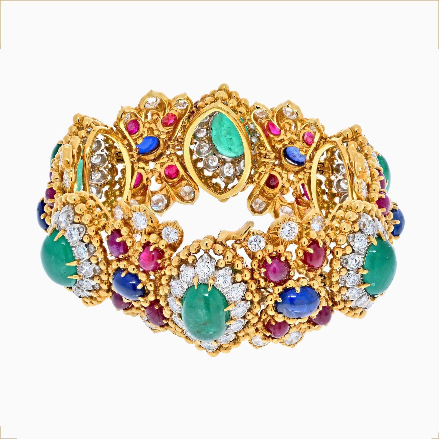 This is a spectacular and exciting David Webb 18K Yellow Gold gemstone bracelet with diamonds. The gemstones include emeralds, sapphires, and rubies that are further decorated with diamonds. Gems are of cabochon cut and form a floral layout