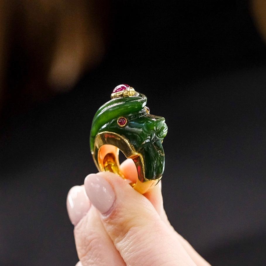 Modelled as a lion, the carved nephrite body accented with cabochon ruby eyes, mounted in yellow gold, signed Webb.
Stone Dimensions (mm): Length 27.25, Width 13.75. 
Measurements: Band Width 10.1mm, Ornament Width 25.9mm, Ornament Length 13.8mm