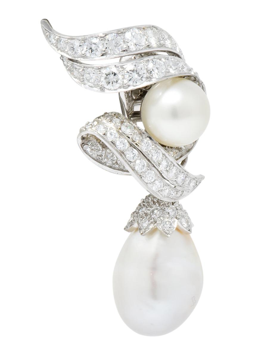 Each features a 10 mm round white pearl with good luster and very pale pink overtones

Numerous bead set round brilliant diamonds surround the central pearl and adorn the bale of the drop

Platinum setting features stylized and dimensional scrolls,