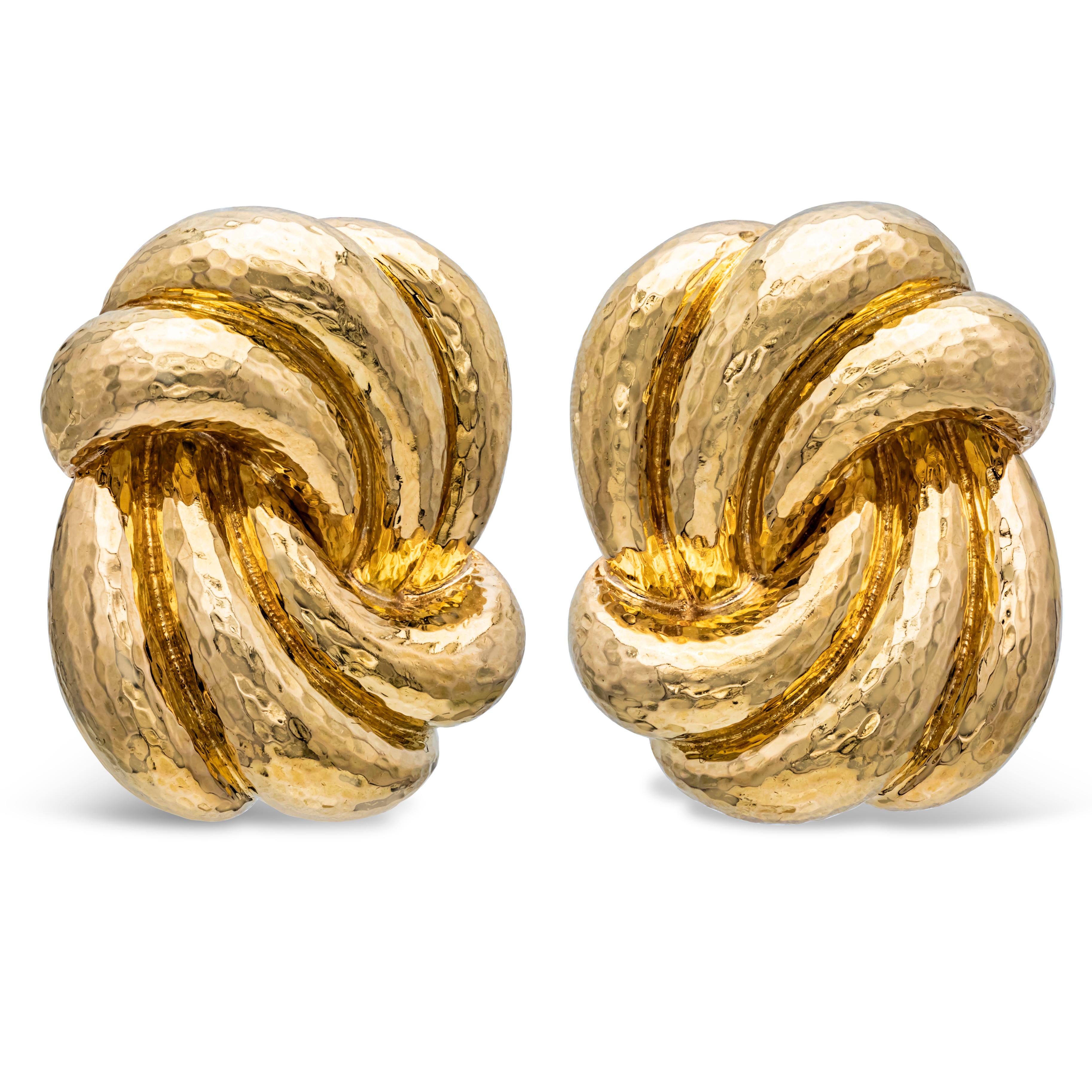 A stunning pair of David Webb earrings, featuring large 18K yellow gold knots with a hammered finish design. Created during the mid-20th century, these ear clips weigh a substantial 41.78 grams and measure 1.3 inches in length, 1 inch in width, and