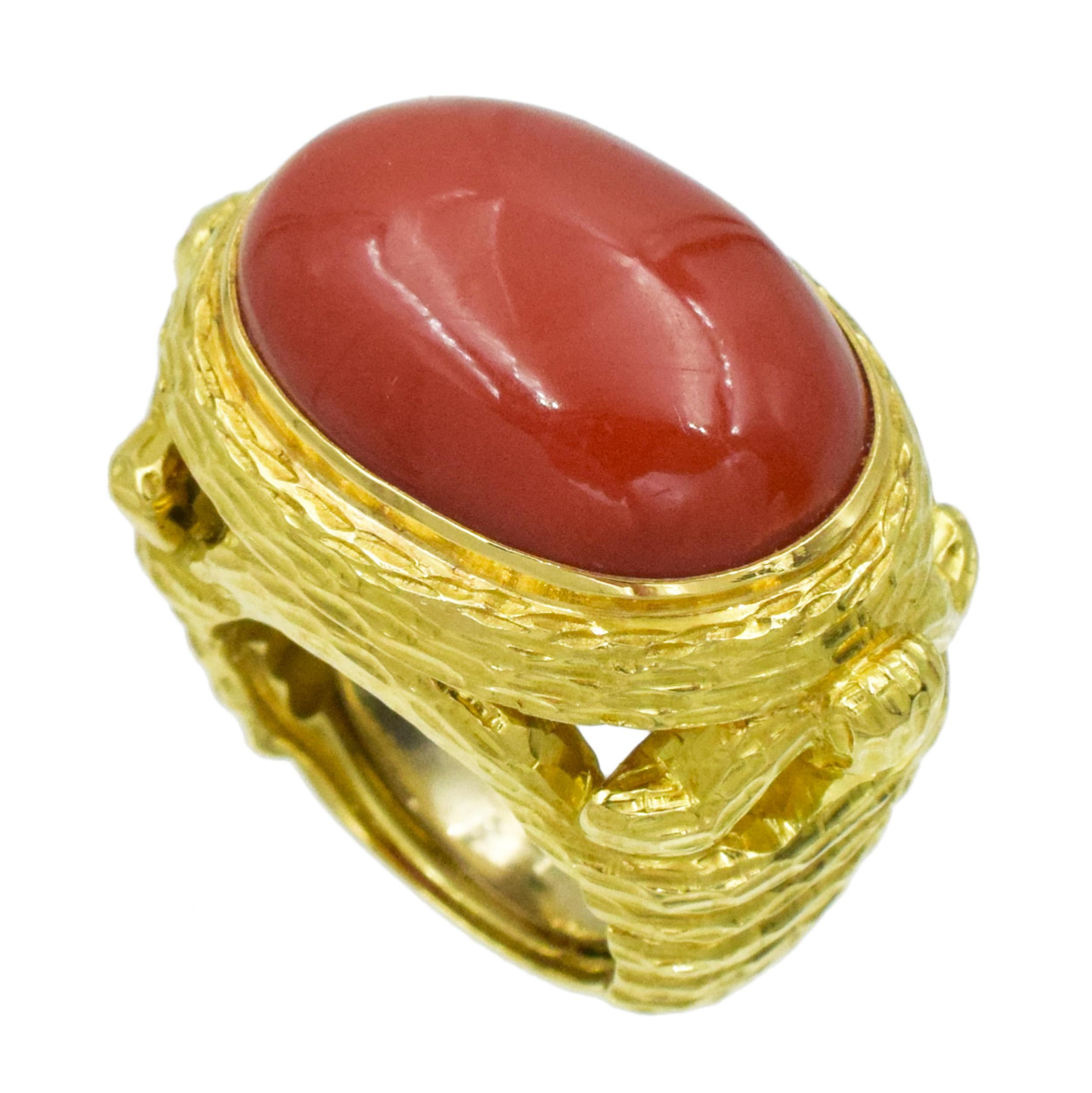 David Webb coral cocktail ring in 18k yellow gold.
Center of the ring features horizontally set oval cabochon cut red coral, measuring approximately 23mm by 17mm, bezel set in 18k yelloow gold decorative mounting. Sides of the ring accented with