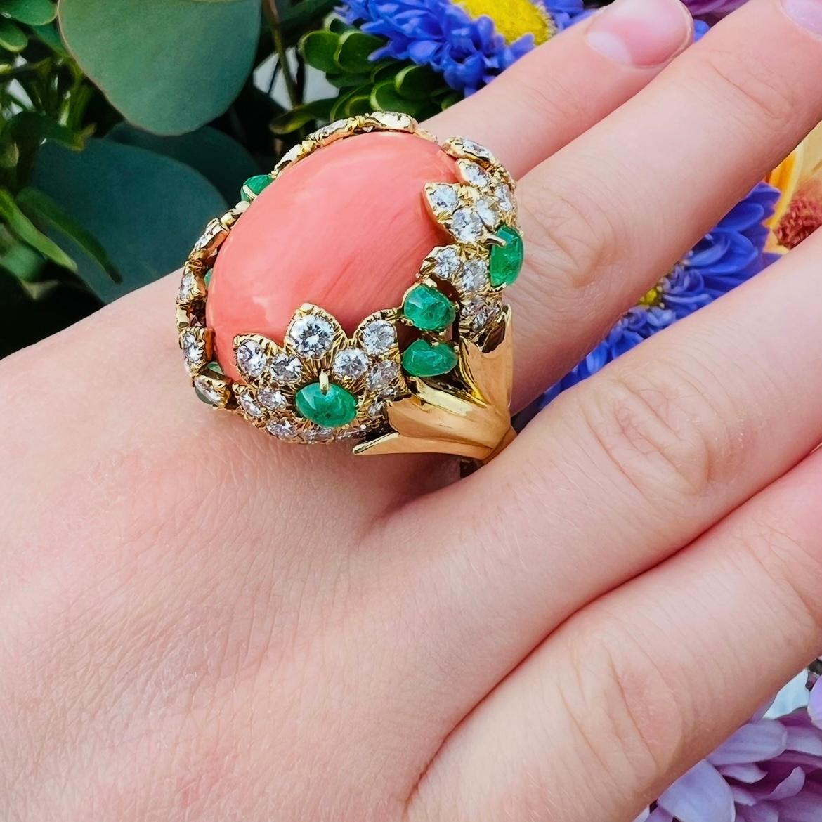 From the creative mind of David Webb comes this stunning coral ring highlighted with emerald and coral accents. The 18 karat yellow gold beauty features a large salmon colored cabochon coral expertly set amongst 4.70 carats of fine white natural