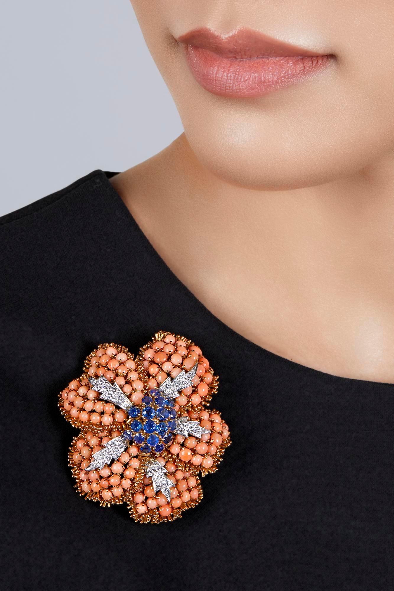 A chic David Webb brooch-pendant of floral design, centering round sapphires, the petals composed of coral cabochons decorated with round diamonds. Measures approximately 2½ x 2¼ inches. Gross weight approximately 39 dwts. Made in the USA, circa