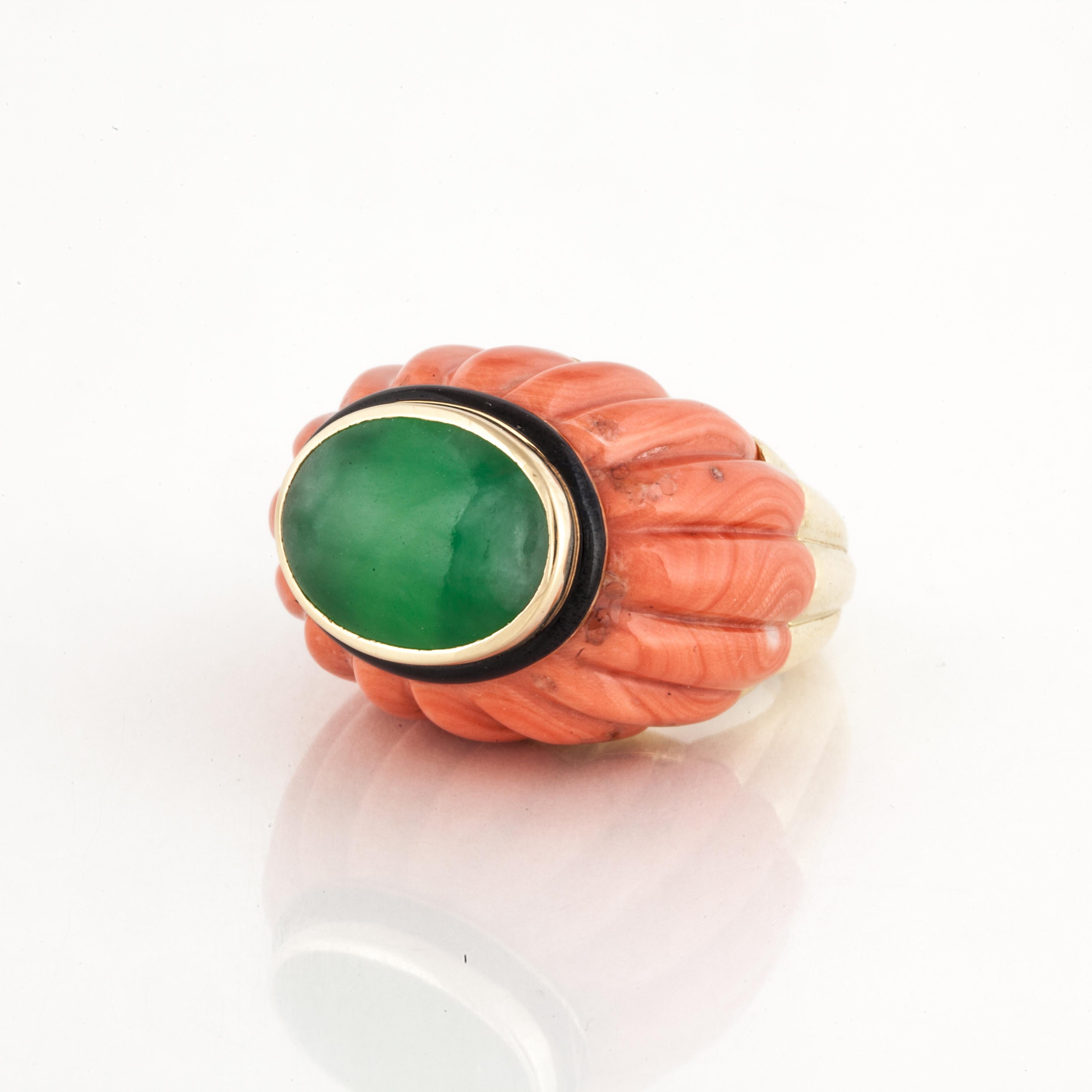 18K yellow gold jade and coral ring by David Webb.  Features an oval polished piece of jade in the center.  Black enamel highlights the coral and jade.  The base of the ring is a single piece of carved coral.  Ring is currently a size 6 with a