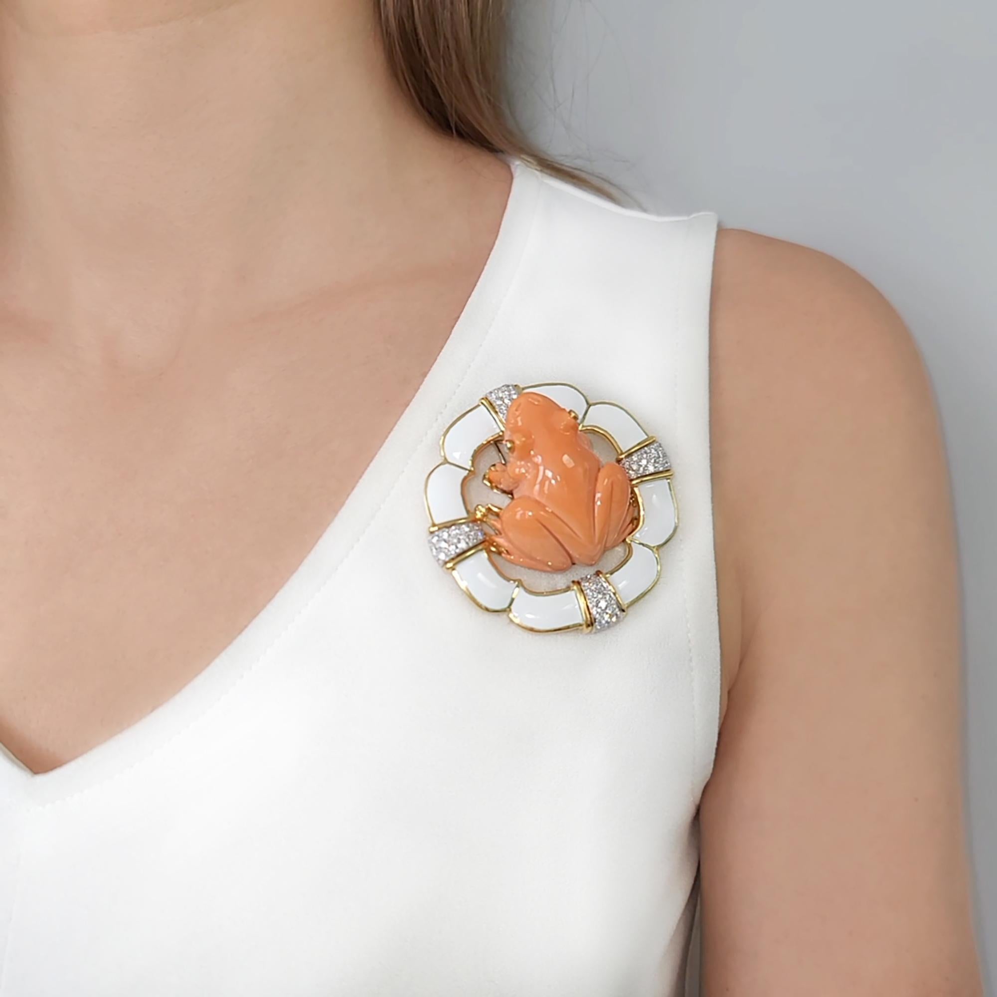 David Webb Diamond, Coral & White Enamel Frog Brooch.
The brooch features coral carved into a frog, accented with bezel set round brilliant cut diamond eyes. The frog rests on 18k yellow gold lilly pod, inlaid with white enamel and accented with