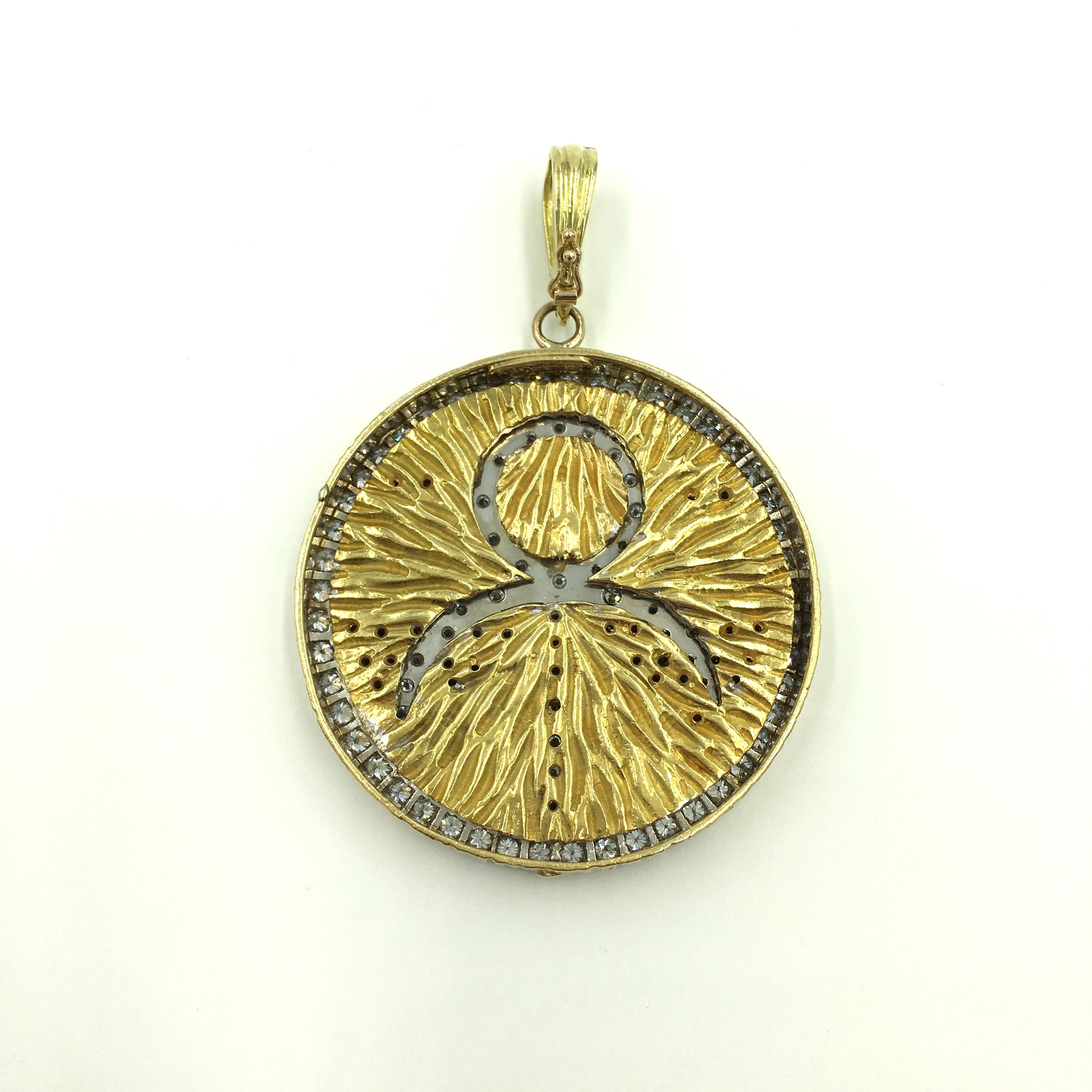 An 18 karat yellow gold, platinum and diamond pendant. Webb. Circa 1970.  Designed as a textured gold disc, depicting the zodiac sign for Libra, enhanced by pave set diamonds, suspended from a fluted gold hinged bale. Diameter of pendant is