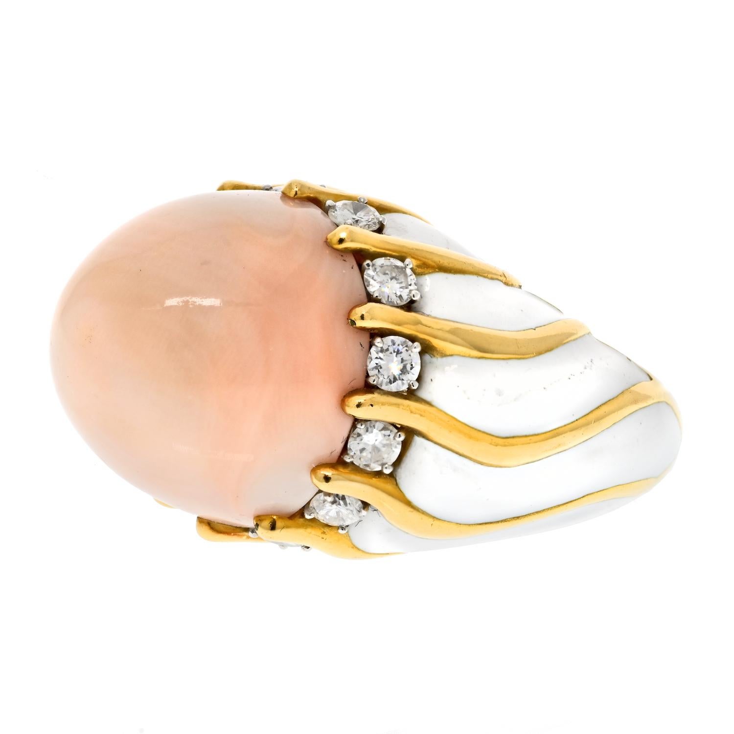 The David Webb 18k yellow gold and white enamel vintage cocktail ring is a stunning piece of jewelry that features a large angel skin coral cabochon cut in the middle, which is further embellished with sparkling white round cut diamonds. This fine
