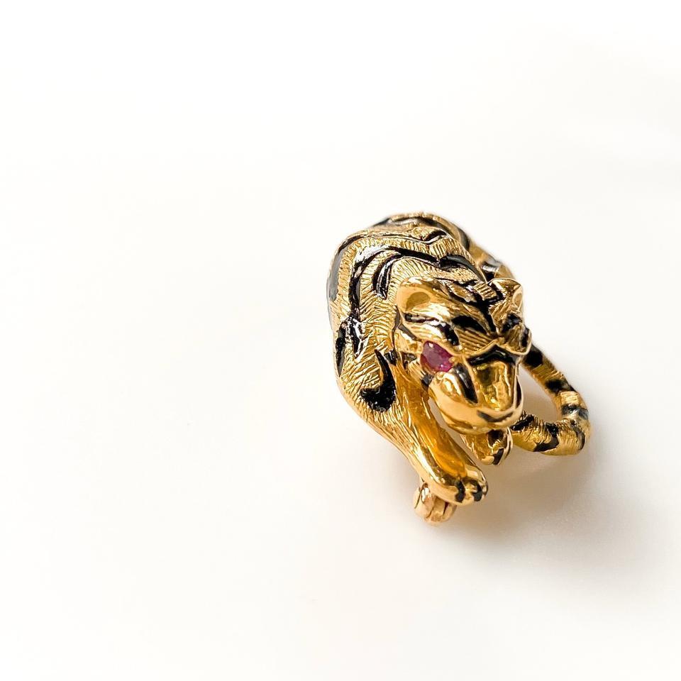 Designed as a textured gold tiger, accented by black enamel stripes, with burnich-set ruby eyes, mounted in 18K yellow gold, length about 1 inches (30mm).
Backing: Single pin with a C-clasp.

Signed 'Webb' for David Webb