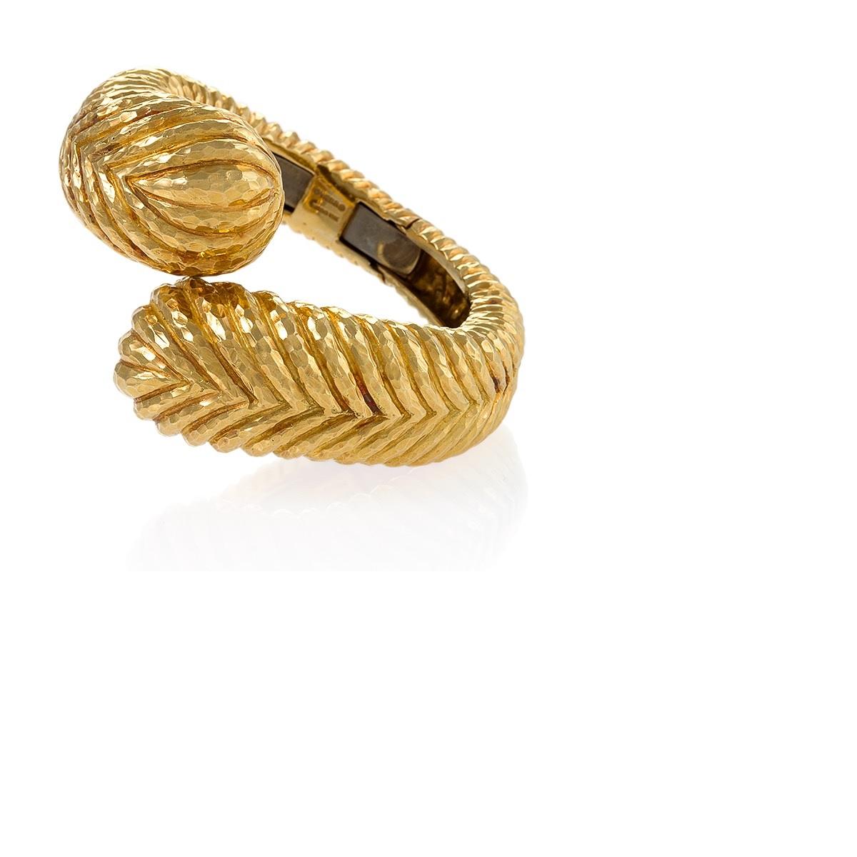 An American Late-20th Century 18 karat gold bracelet by David Webb.  The hinged bracelet is composed of hand hammered gold in a dimensional crossover feather motif.  Circa 1980's.
