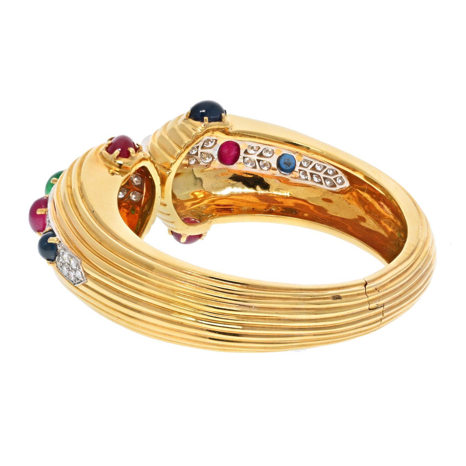 David Webb: made of 18k yellow gold this bracelet is of a hinged design. Fits as if it's a bangle with an easy mechanism to put it on and off. 
Encrusted with beautiful gems like rubes, sapphires and emeralds of oval cabochon cut as well as a touch