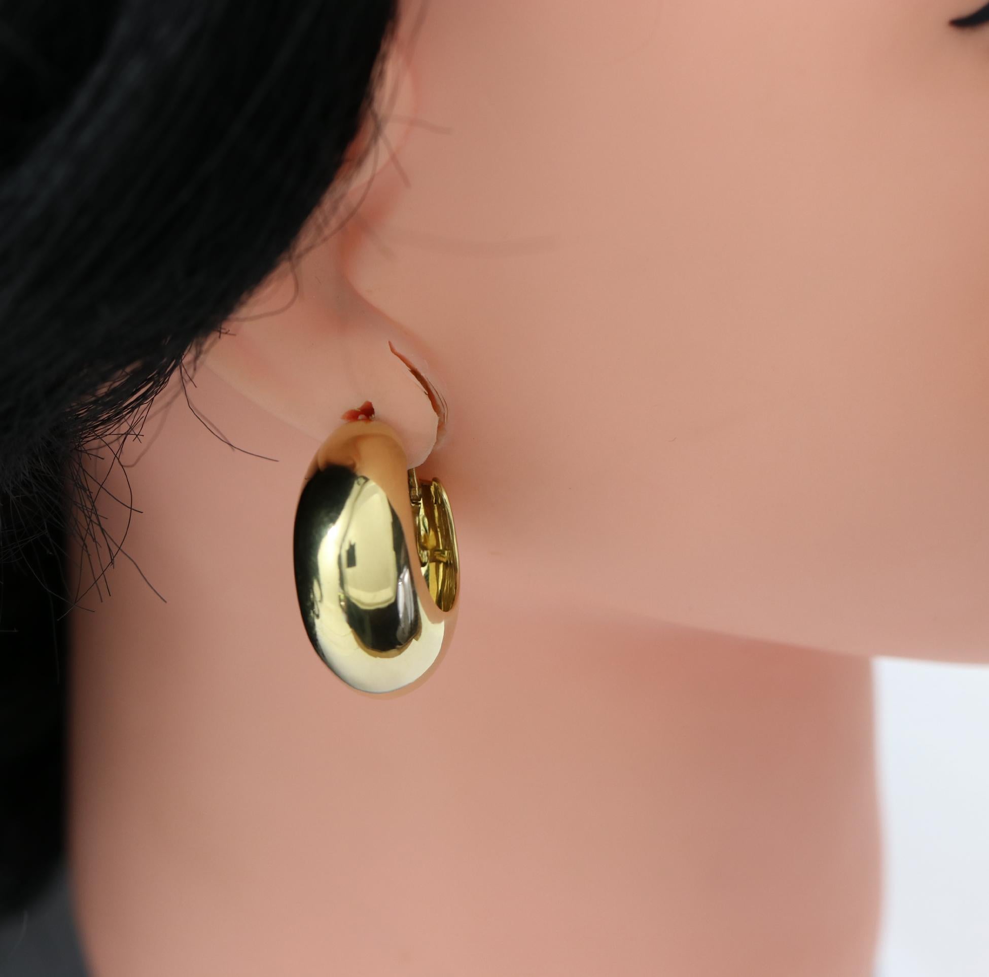 A pair of high polished 18K yellow gold hoop earrings measuring 1/2 an inch wide, and 1 3/16 inches in diameter. Perfect for daytime or casual wear with a classy look. Signed 