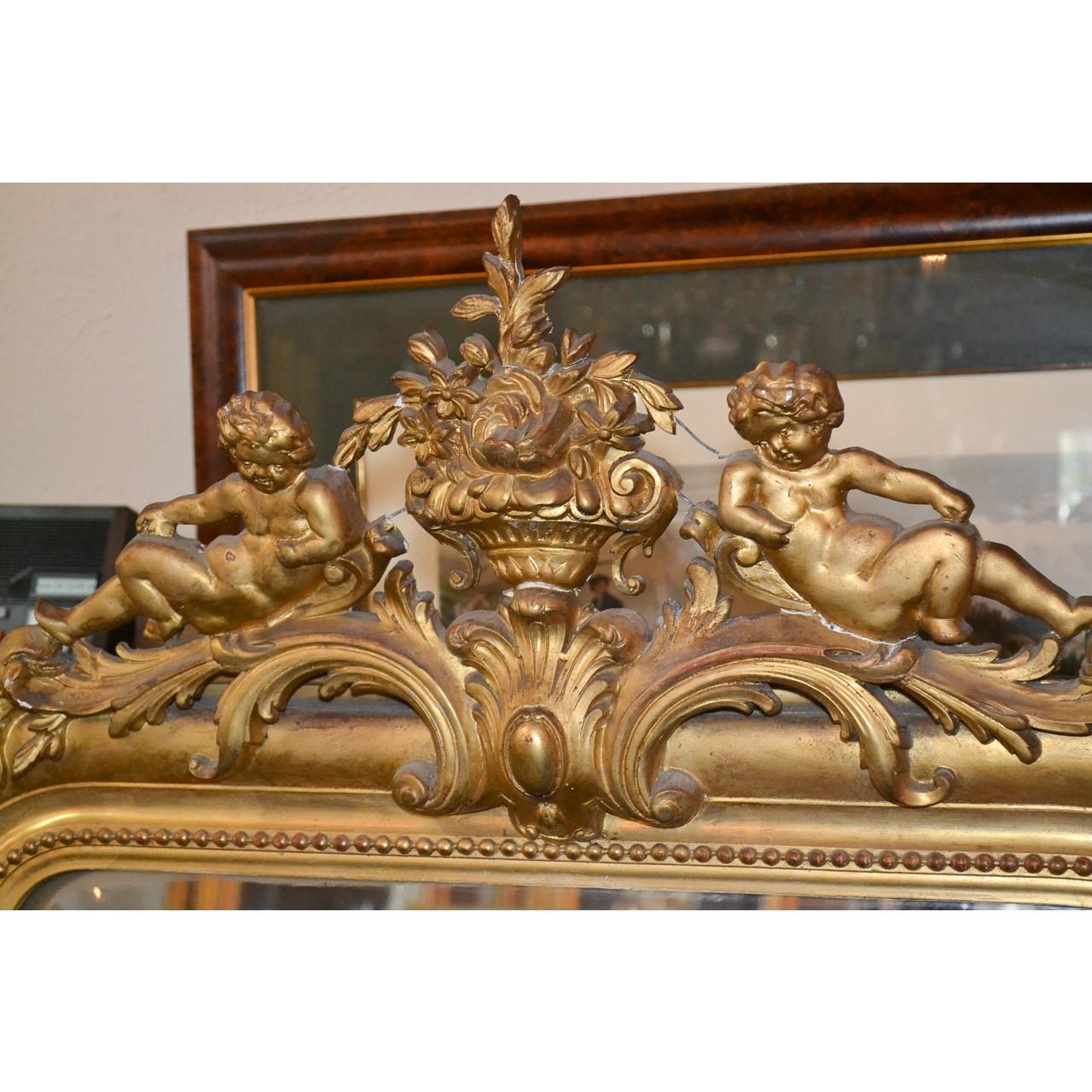 Exquisite 19th century French Louis Philippe carved wood and gesso beveled edge console or wall mirror with a gold-gilt finish. The finely detailed crest decorated with a floral urn flanked by cherubs resting upon scrolling leaves. The frame