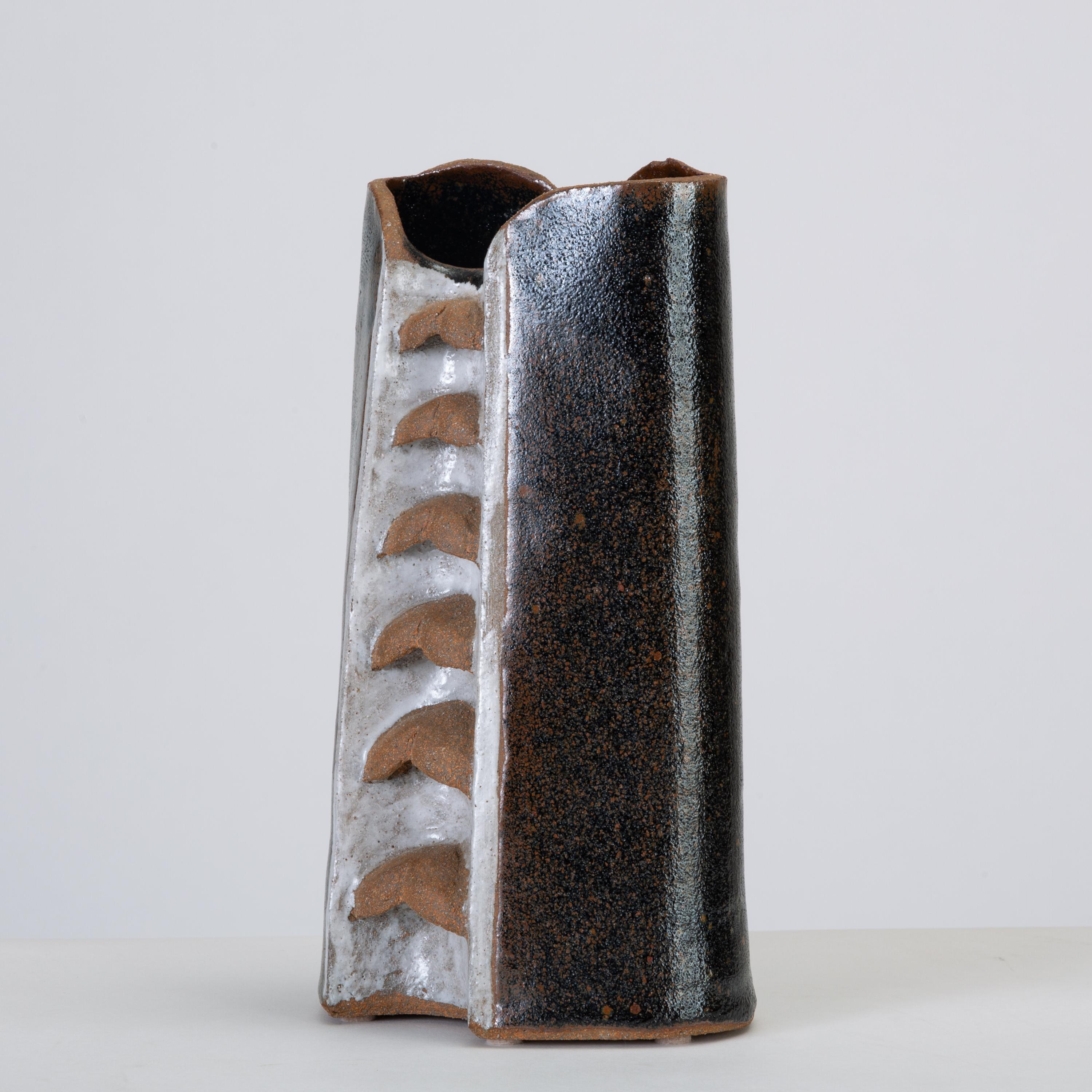 A sharply modern handmade vase from the 1990s. The angular, geometric vessel has a glossy black finish with a contrasting central panel in bright white with a row of unglazed ridges in natural stoneware. Signed by artist 