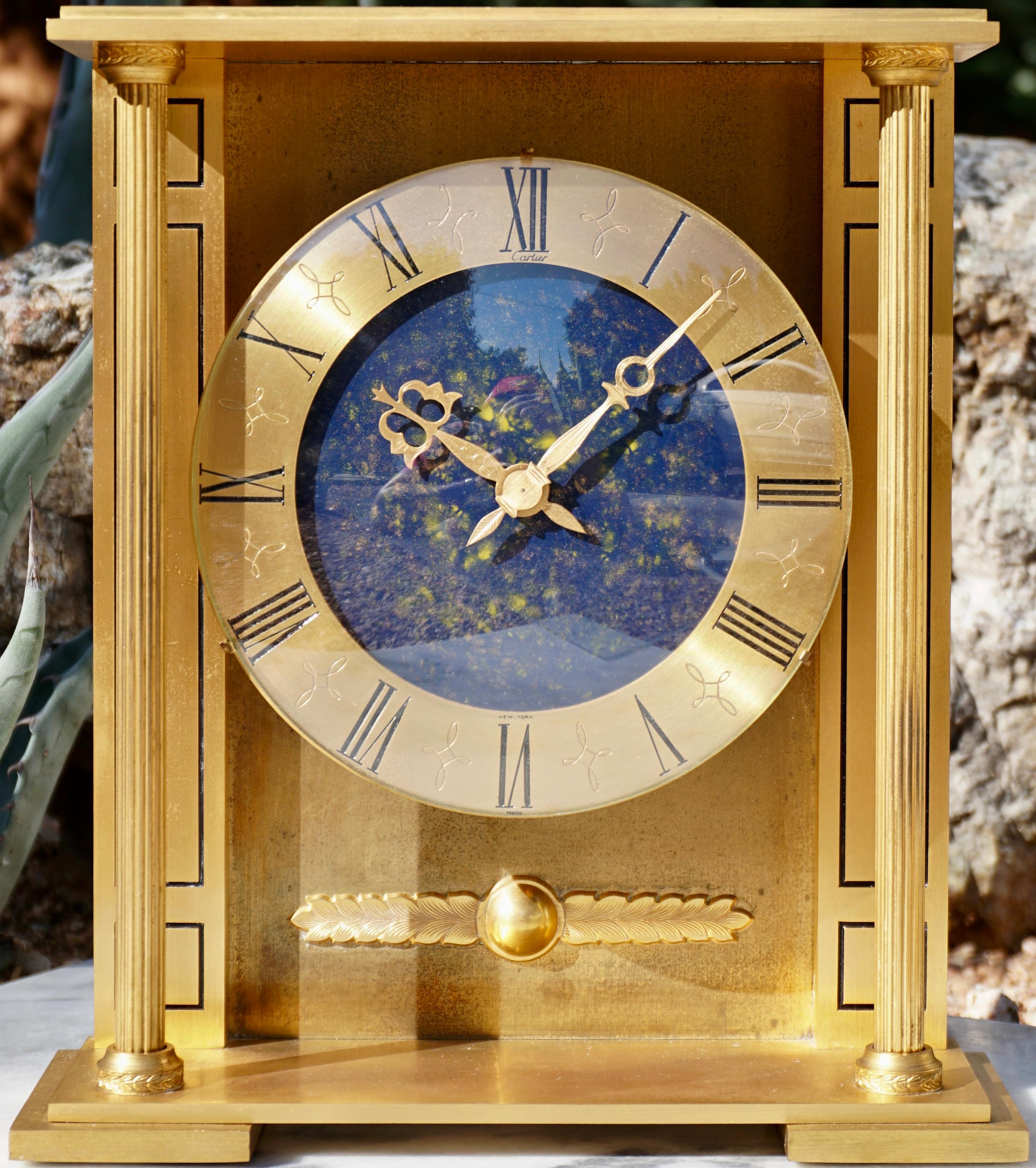 Expert craftsmanship! A rare and important Cartier mantle or desk clock of heavy gilt gold bronze with a polished Lapis Lazuli cobalt blue and yellow gold inclusions. Of classical carriage decorative design with columns and a Greek winged eye touch.