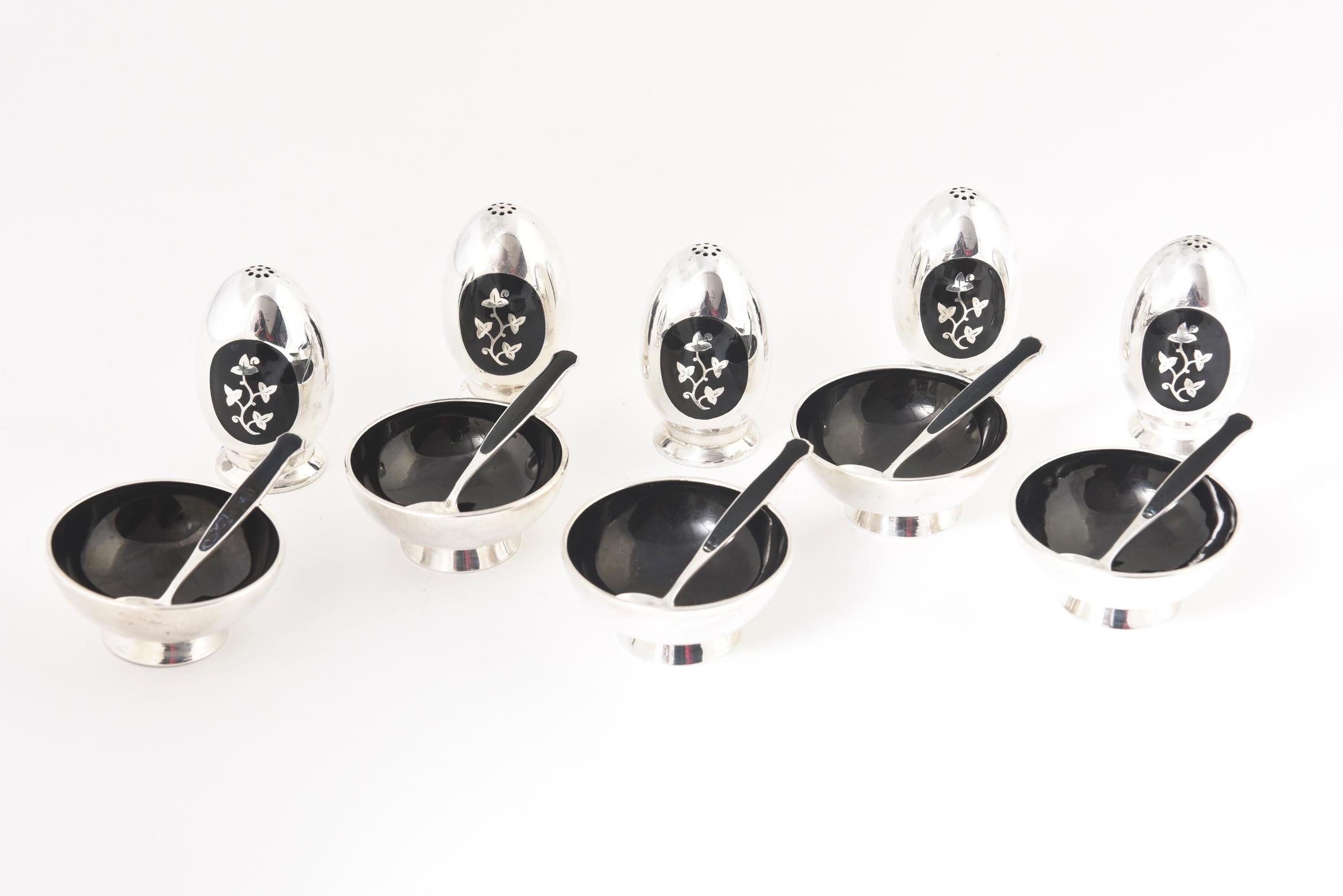 Elegant mid 20th century moderne sterling silver and black enamel salt and pepper sets by Danish designer Meka. There are 5 sets each has a pepper shaker, a salt bowl and a matching spoon. 

The bottom of one of the peppers is missing. You could