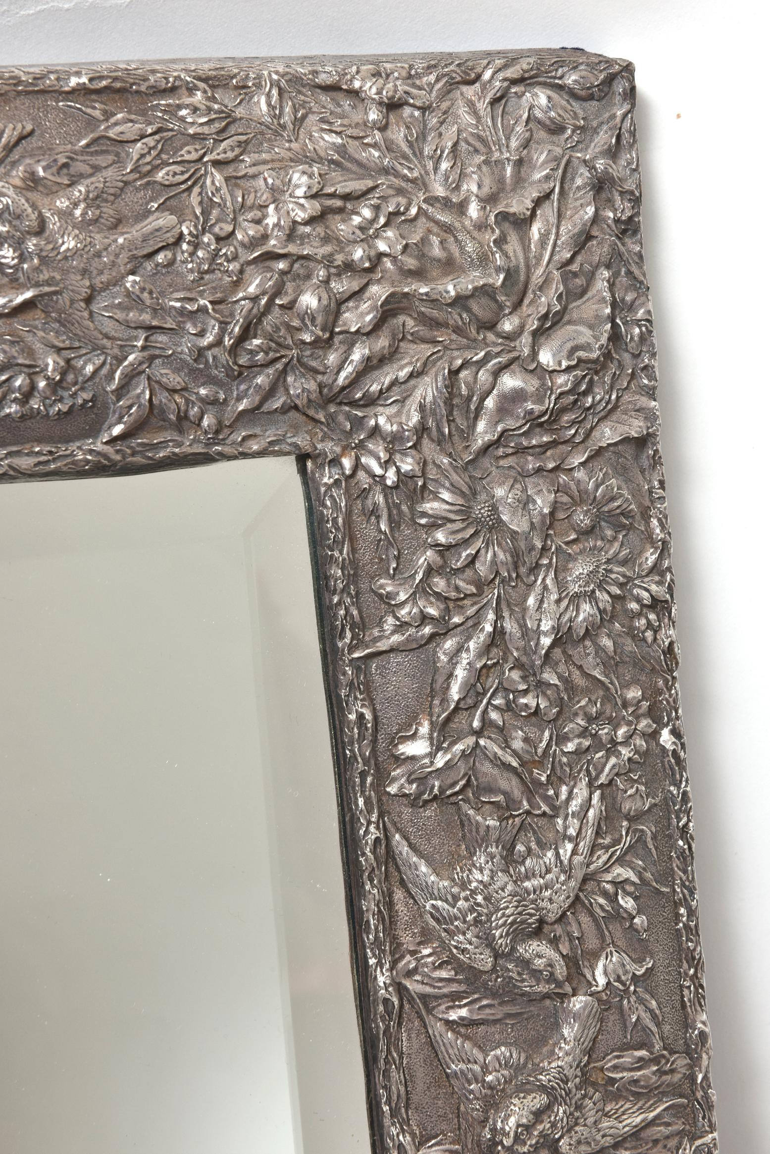 20th century, large sterling silver repoussé frame decorated in the Aesthetic style with birds flying amidst flowers. Inside the frame is a beveled glass mirror. The backside of the rectangular frame is blue velvet with an easel back. 

 Marked