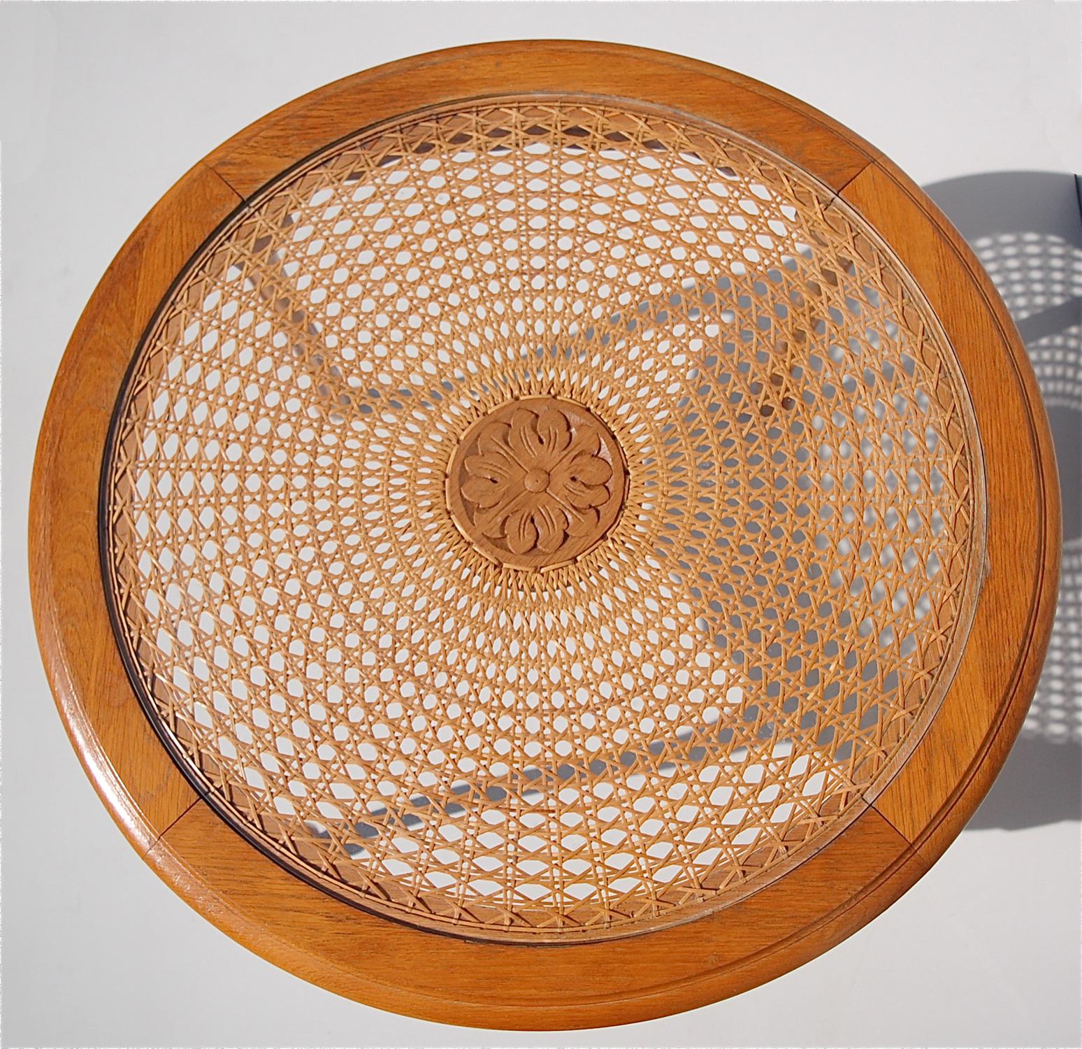 This French, vintage, round coffee or cocktail table has been carved from solid oak. It has a sunburst pattern caned top with a plate glass insert which can be removed. In the center of the cane work is a carved oak medallion. Because of its modest