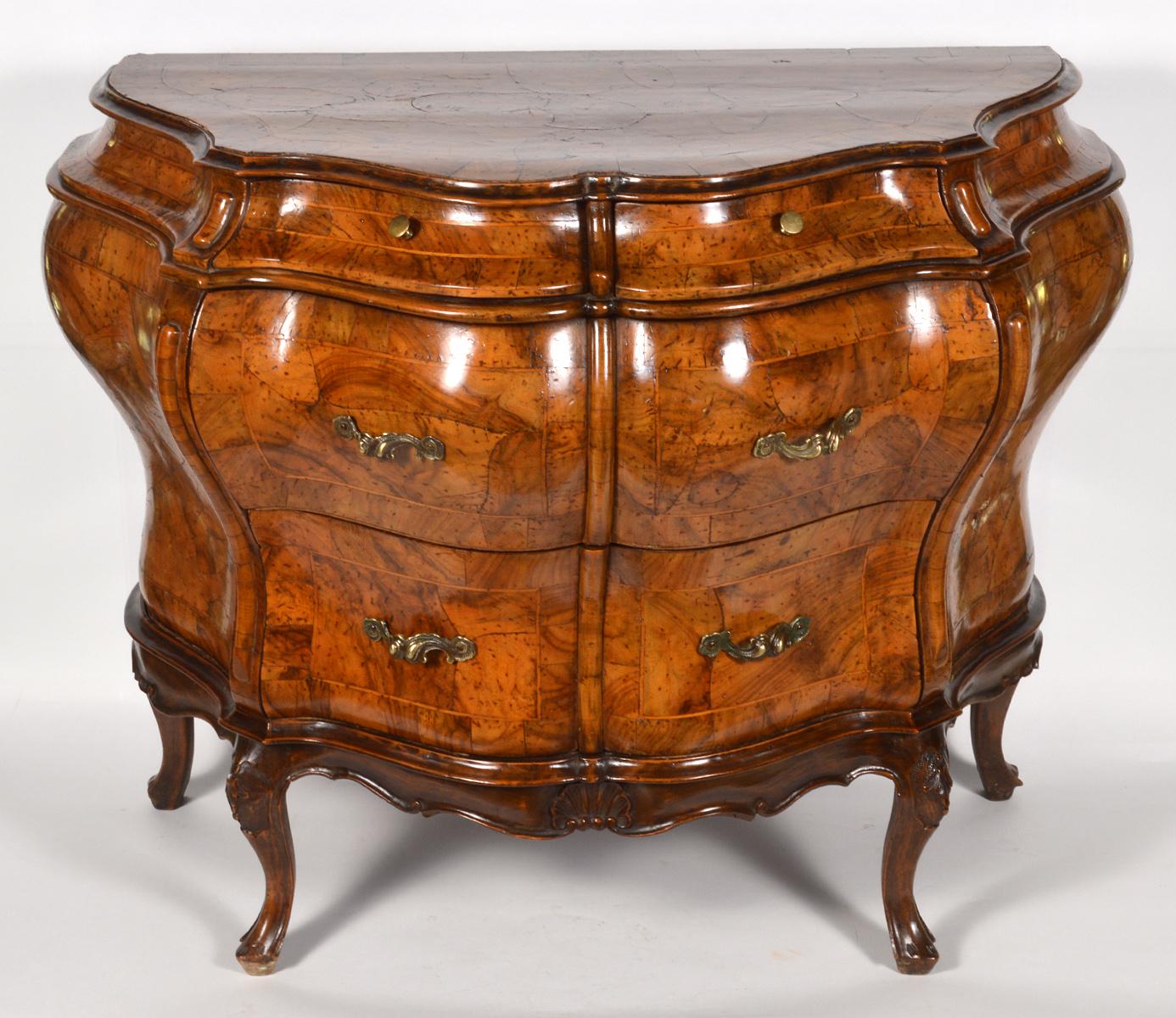 This sumptuous Italian olive wood bombe commode features a banded inlaid top above two frieze drawers and two long drawers resting on a scalloped apron and shaped cabriole legs. The sculptural form is owed to its body being of the compound type