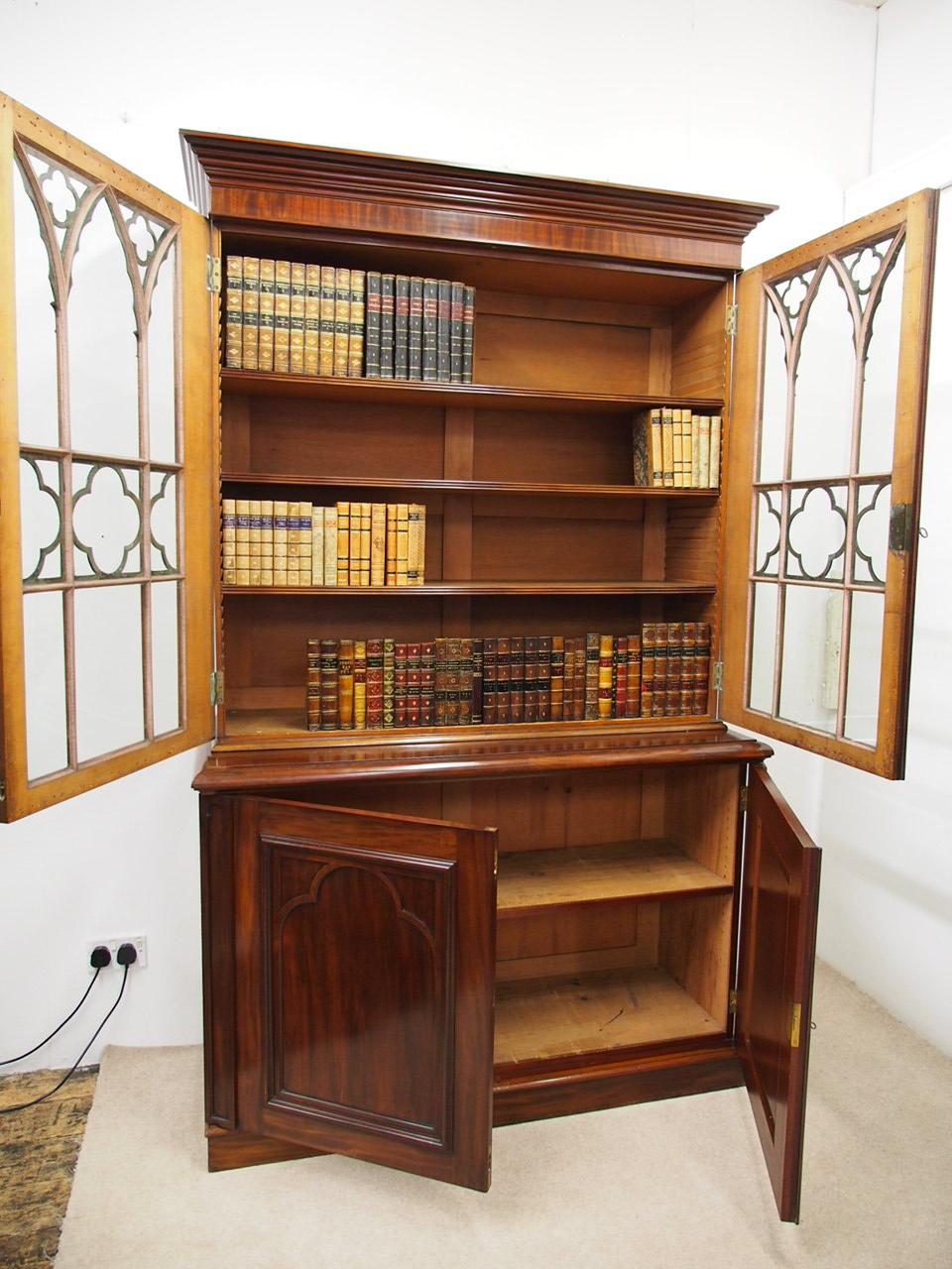 Gothic style cabinet bookcase in figured mahogany, circa 1840. The upper section has elaborate Gothic style astragal bars and carvings surmounted by a simple classic cornice, Gothic style pilasters at the sides and rounded moldings to the frieze. It