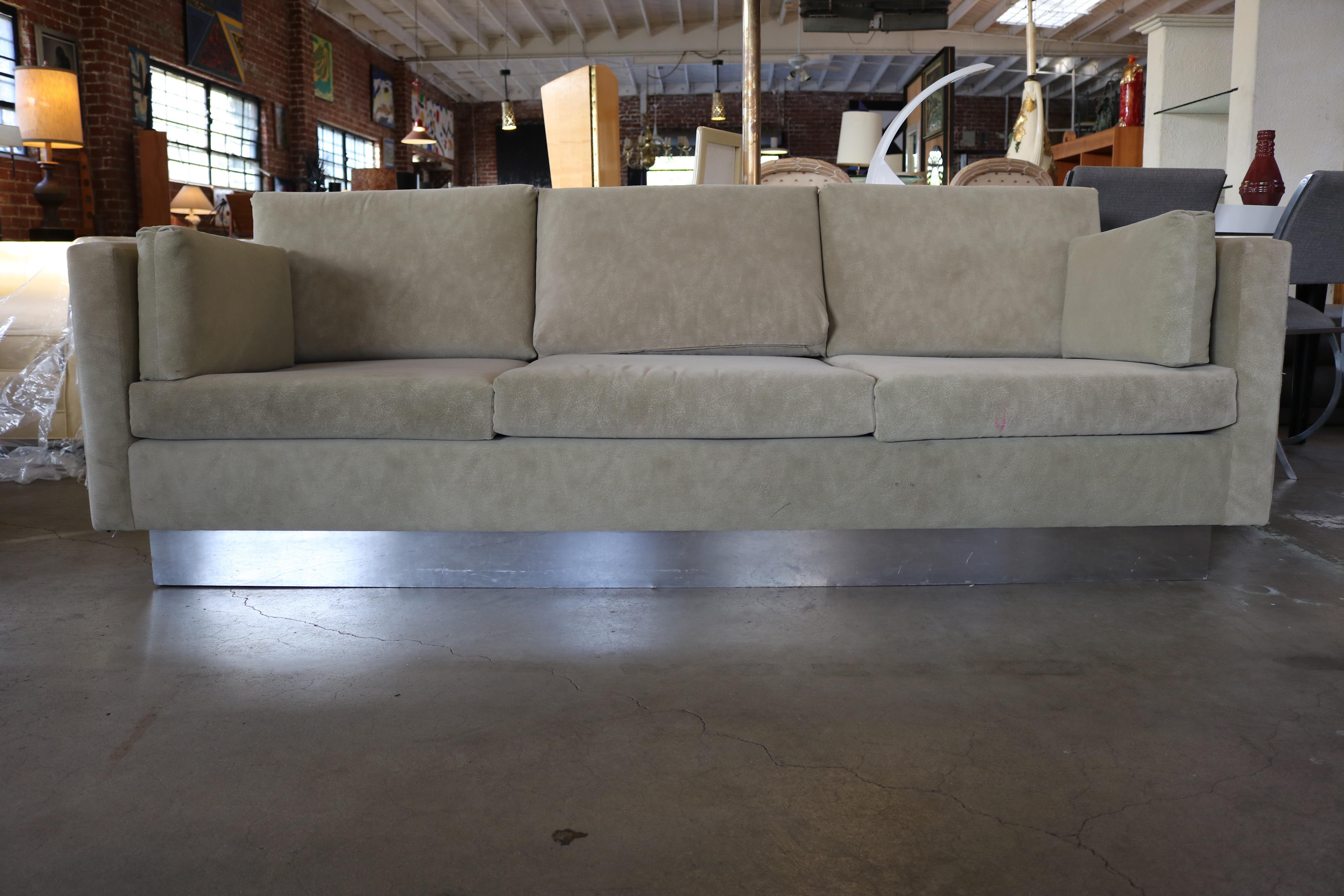 This textured suede light brown three-seat sofa rests on a chrome base, with two side cushions.