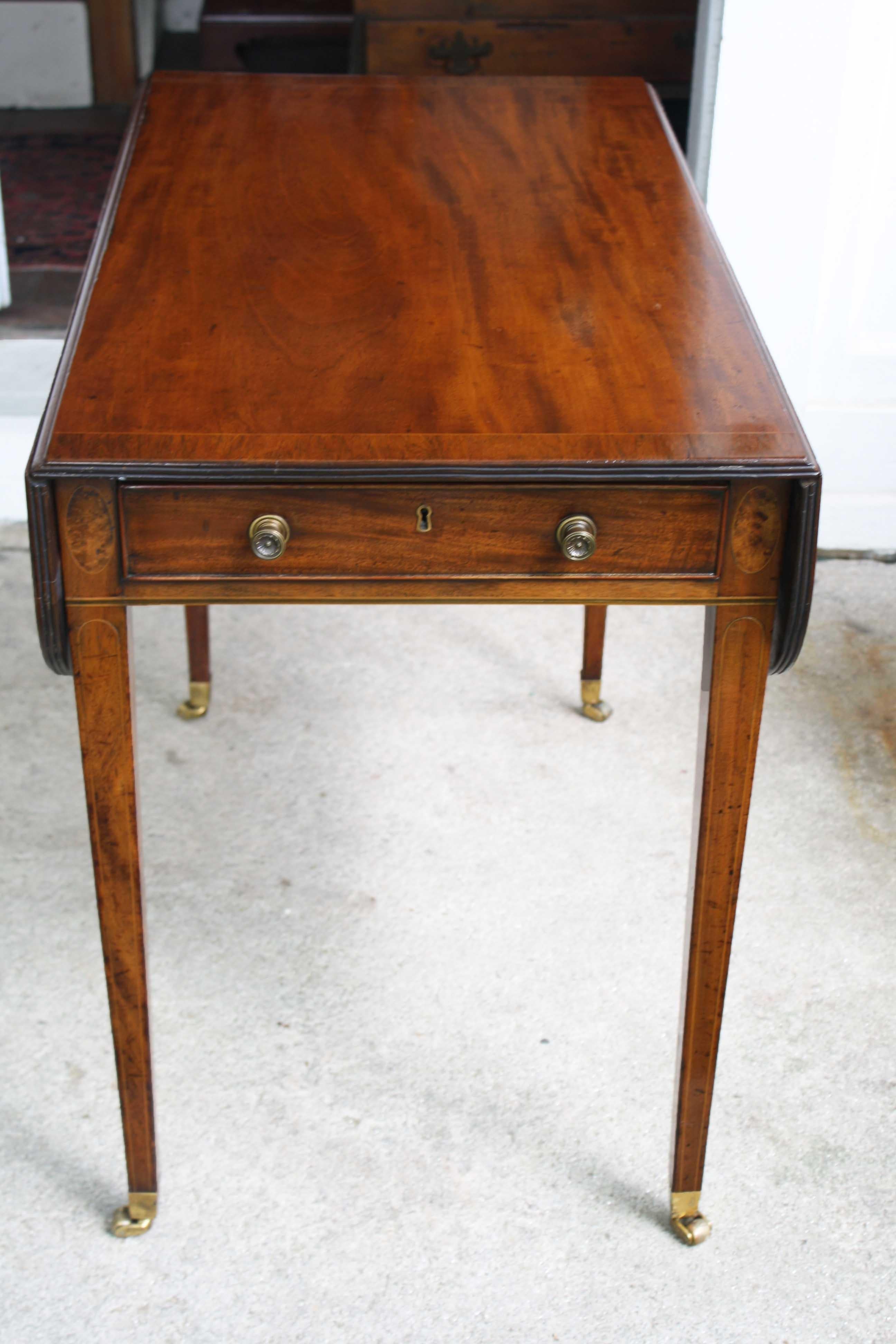 In the Hepplewhite manner, a fine line and ebony inlaid, rosewood banded drop-leaf Pembroke table. Both its functional and faux drawer fronts are beaded and surrounded by elliptical inlays. Brass drawer pulls as well as leg cups and casters appear