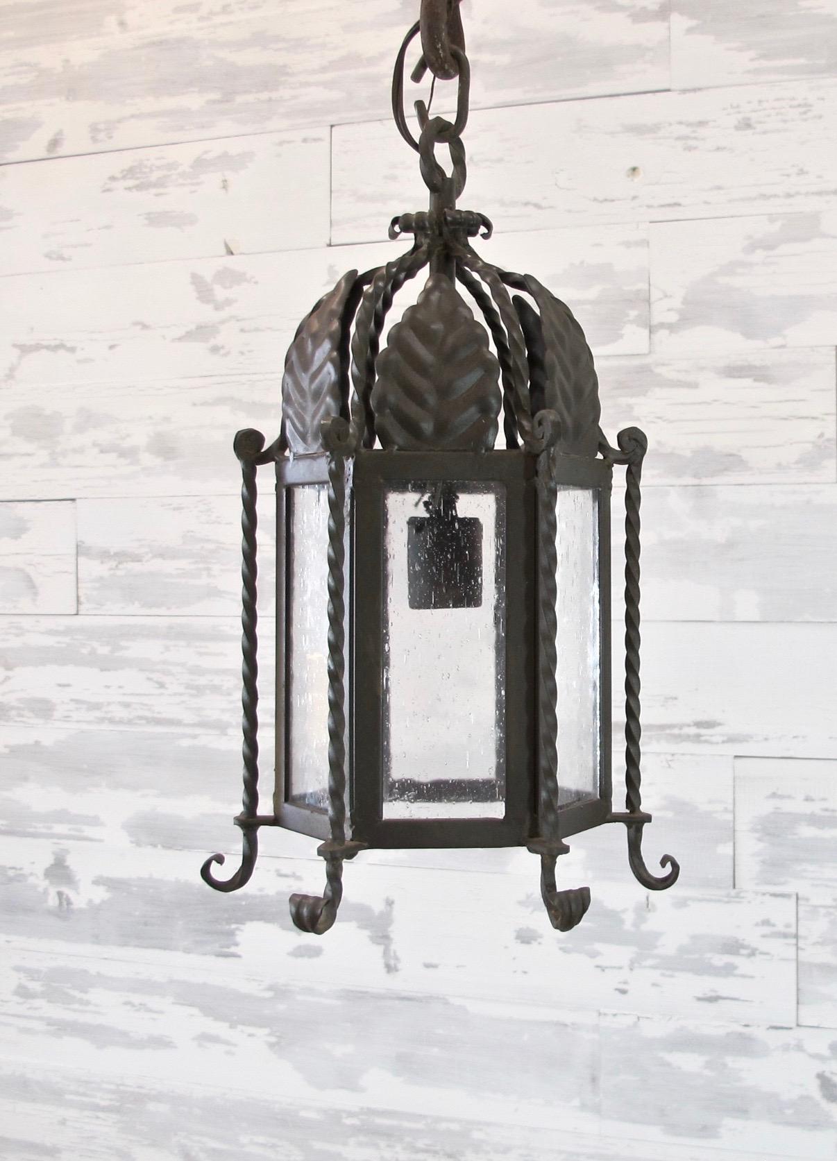 Pair of small forged iron lantern with leaf motif. Iron with seeded glass in antique bronze finish. Scroll details on the bottom. Each has a single medium base bulb up to 60 watts. Wiring is UL listed, chain and canopy included. Measures: 12
