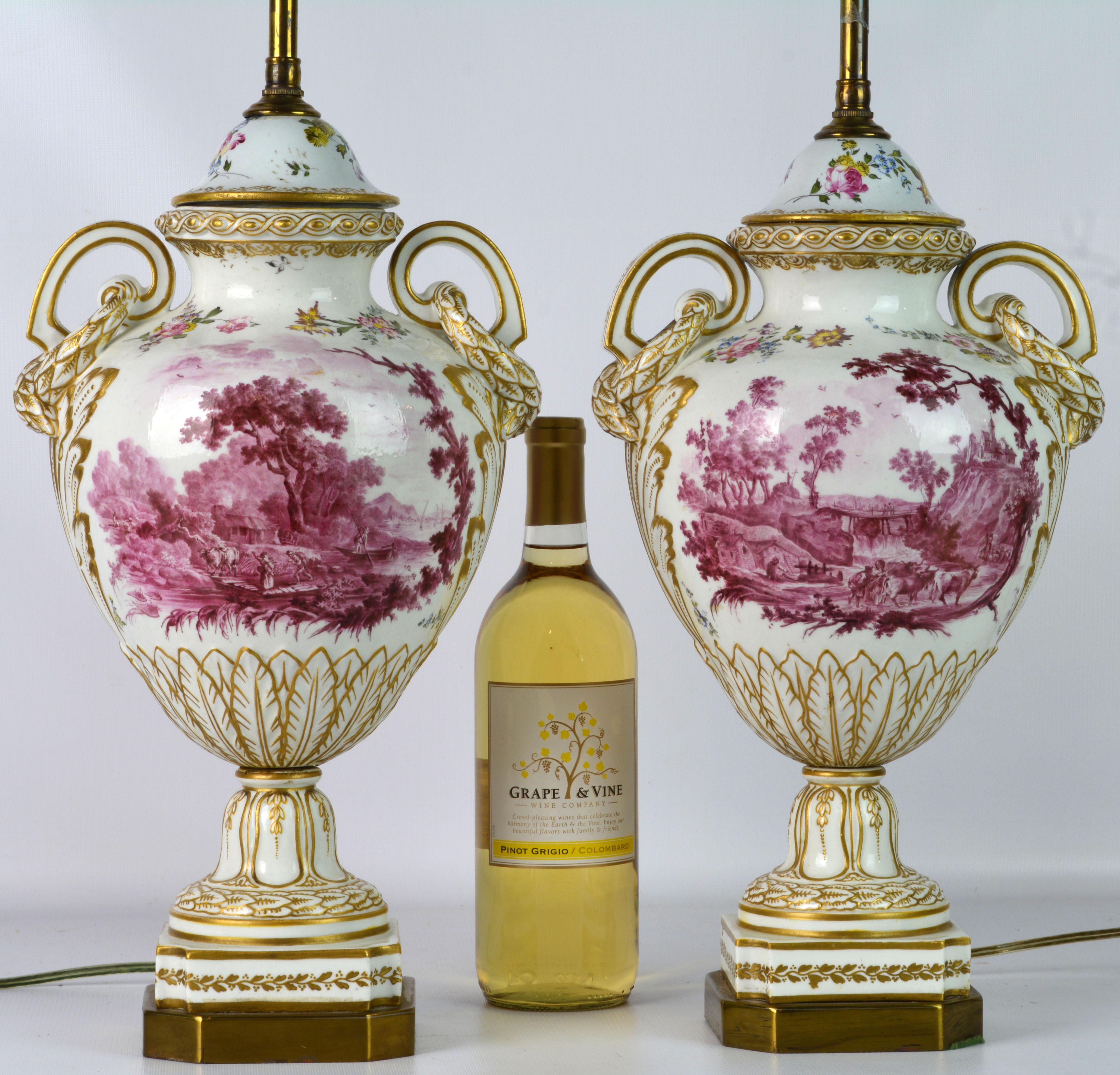 These large French old Paris porcelain lamps feature purple 'puce camaieu' landscape paintings on both sides set on gilt decorated white ground. The form is typical for the Louis XVI style and features elegant laurel draped scrolled handles. The