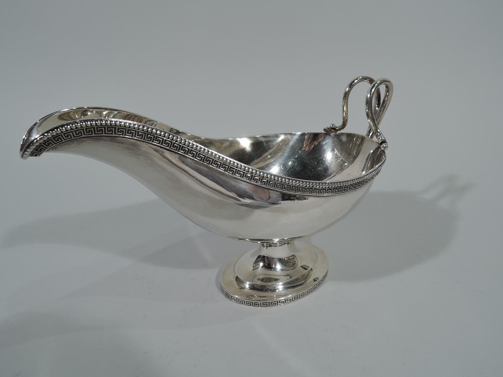 Greek Revival sterling silver gravy boat. Retailed by Tiffany & Co. at 550 Broadway in New York. Elongated bowl with helmet mouth, split and scrolled high-looping handle with leaf mouth, spool stem, and stepped oval foot. Fretwork and beading.