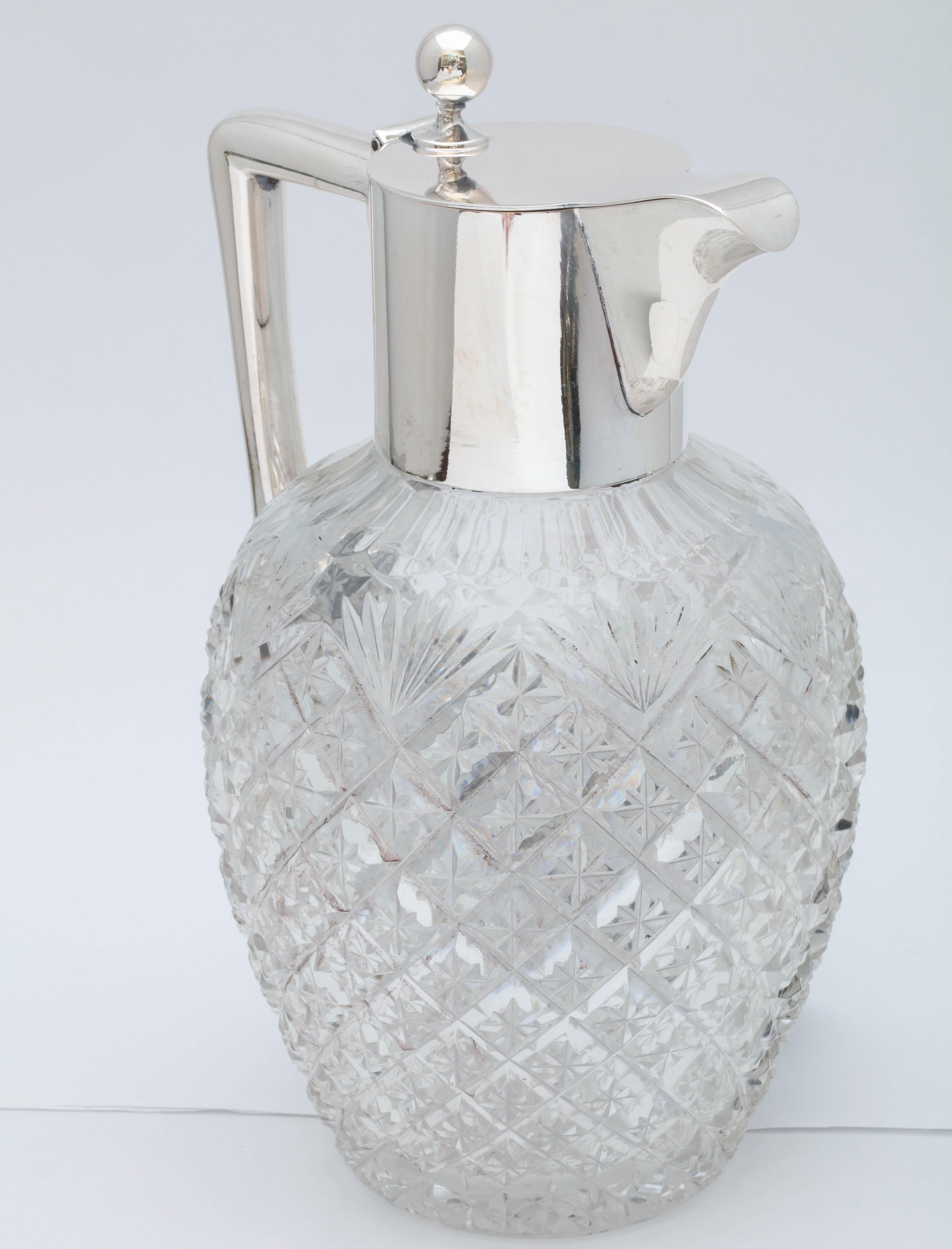 Edwardian, continental silver (.800) - mounted cut glass claret jug, with hinged lid, Germany, circa 1905. Measures 9 inches high to top of finial x 5 3/4 inches wide from outer edge of handle to outer edge of spout x 5 inches deep. Dark spots in